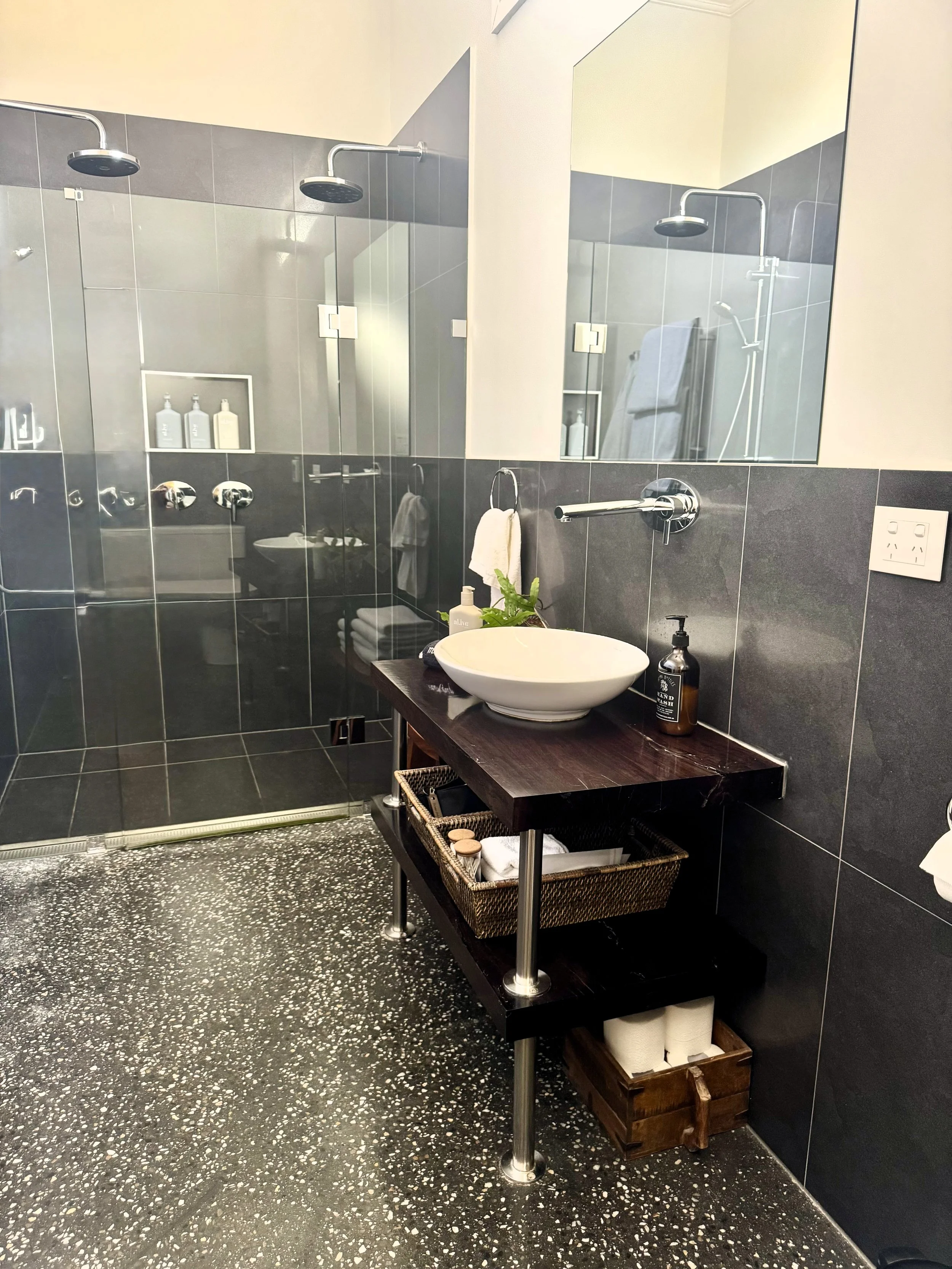 Modern bathroom with a glass-enclosed shower area, a dark wooden vanity with a bowl sink, a mirror, and neatly arranged toiletries and towels.