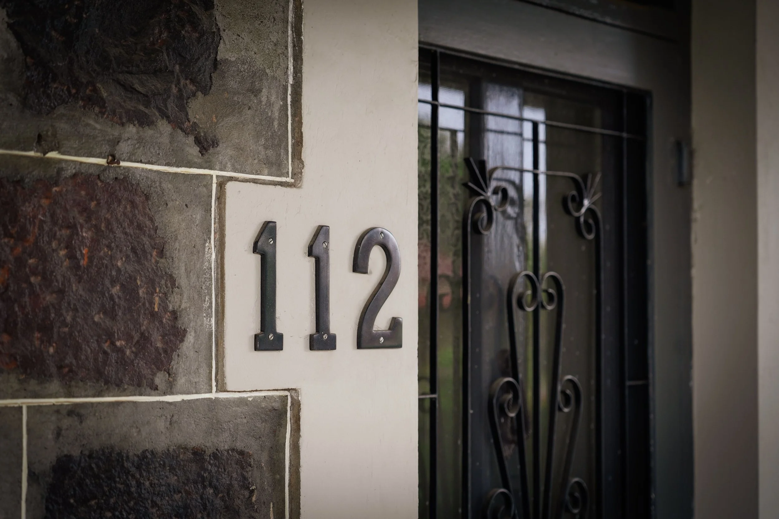 House number 112 on wall next to black decorative metal gate.