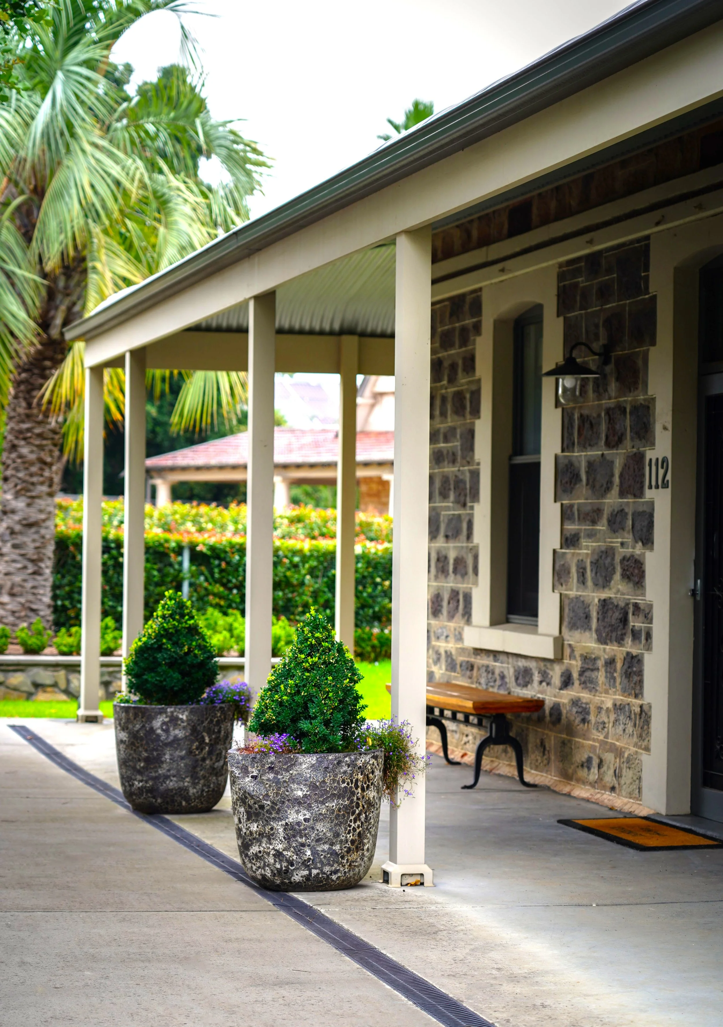 Front porch with stone siding, potted plants, a bench, and a house number 112.