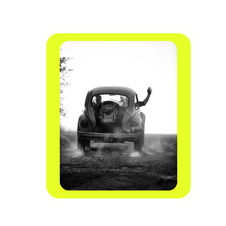 A person waving from the passenger side of a vintage black car driving on a dirt road during daytime.
