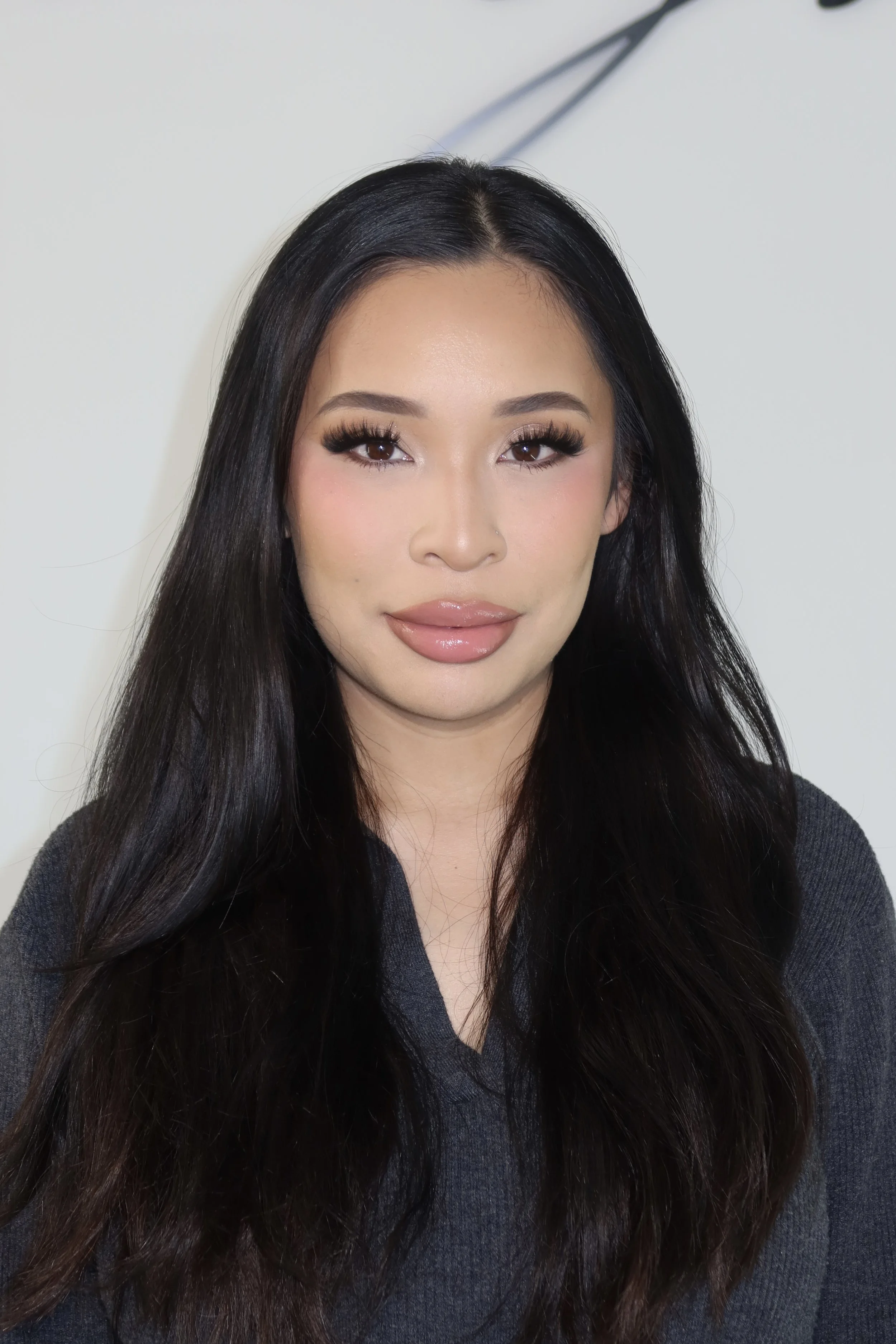A woman with long black hair, makeup, and a gray top looking at the camera.