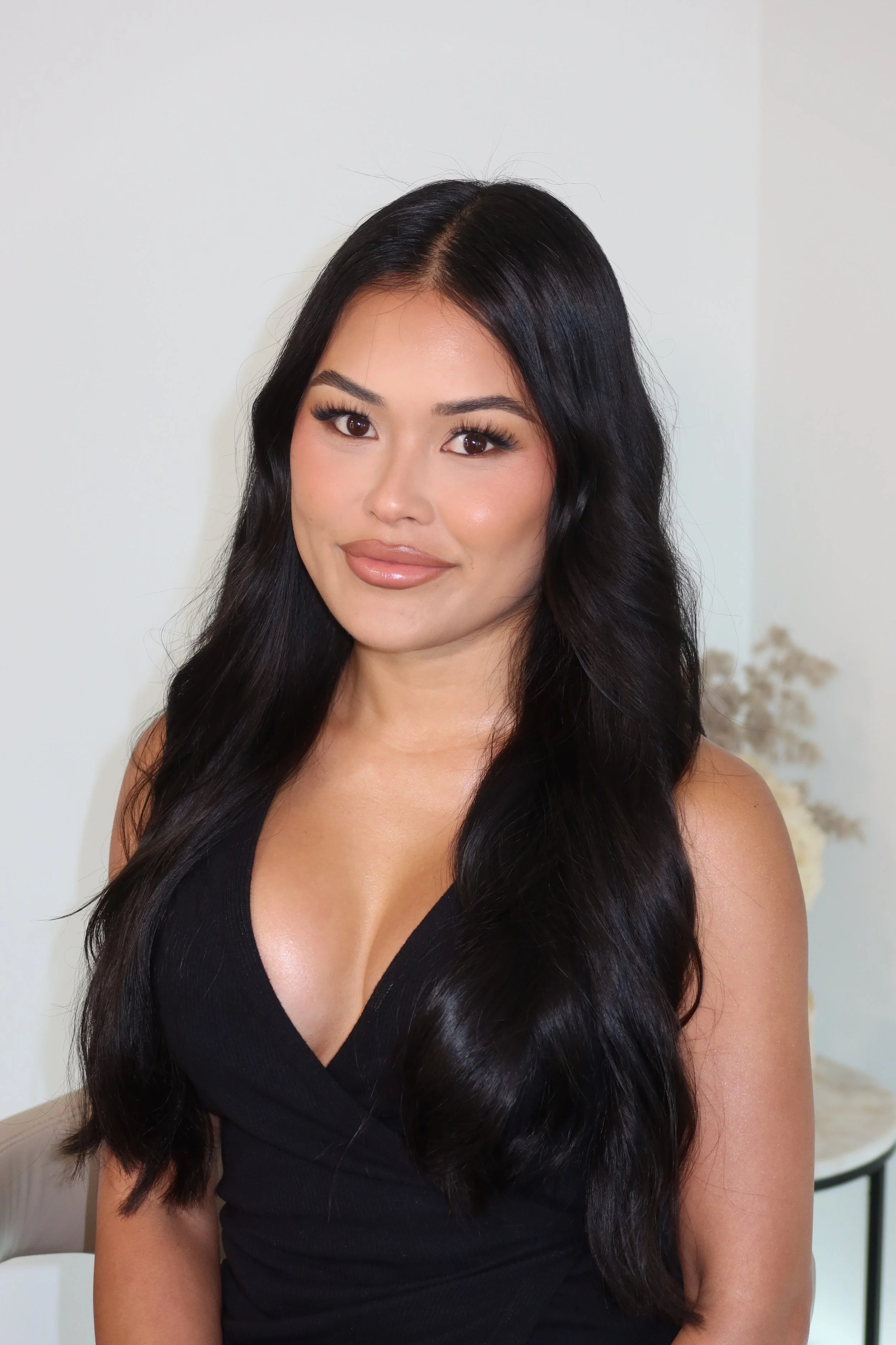 A woman with long black hair, wearing a black sleeveless top, smiling softly at the camera.
