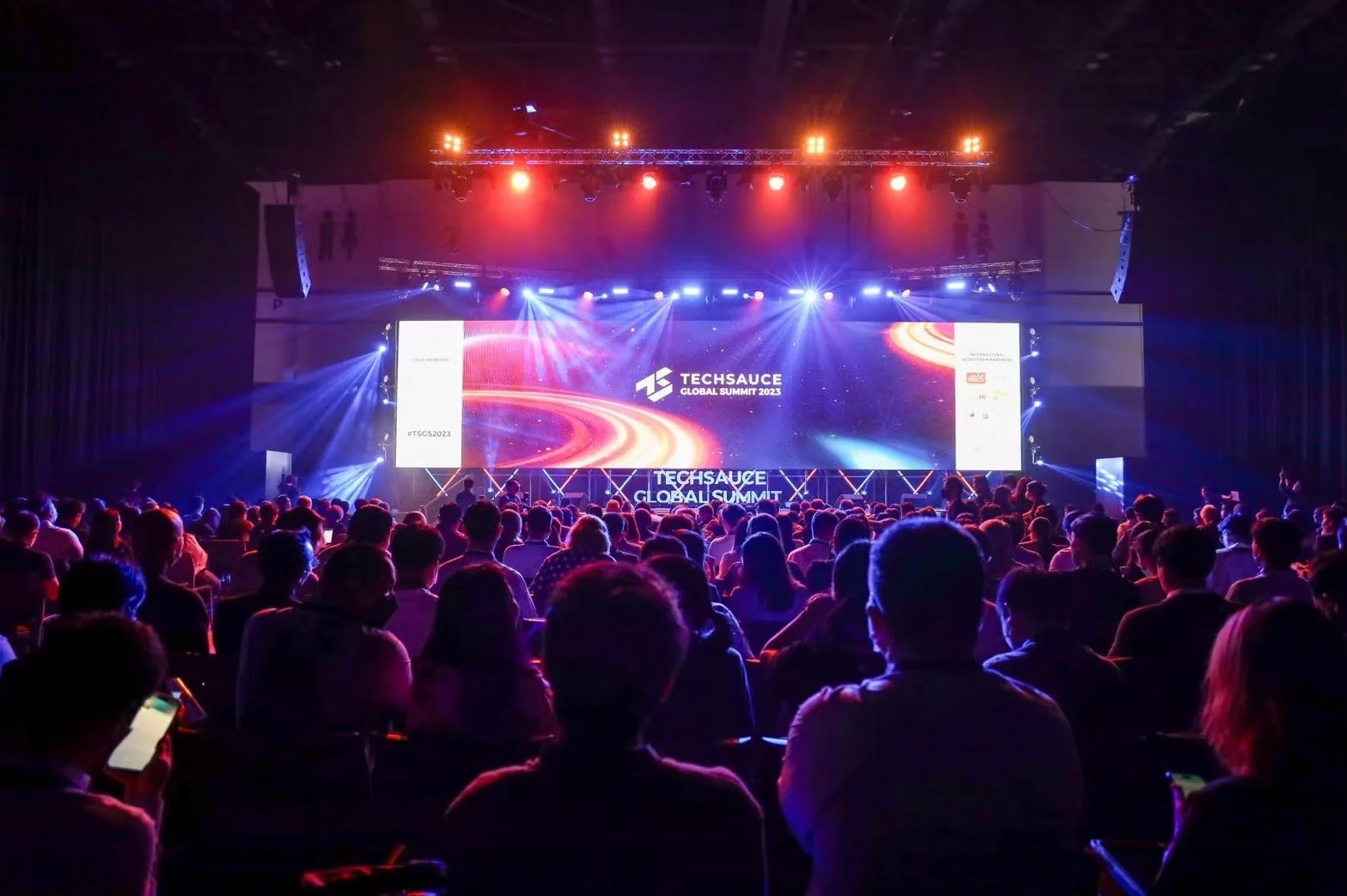 Audience attending the Techsauce Global Summit 2023 with a large, brightly lit stage and screens in a dark conference hall.