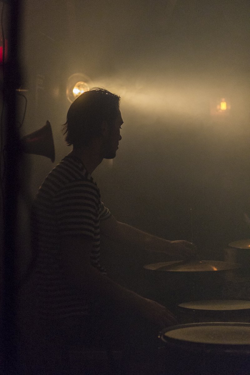 A silhouette of a person playing drums in a dimly lit room with warm lighting.