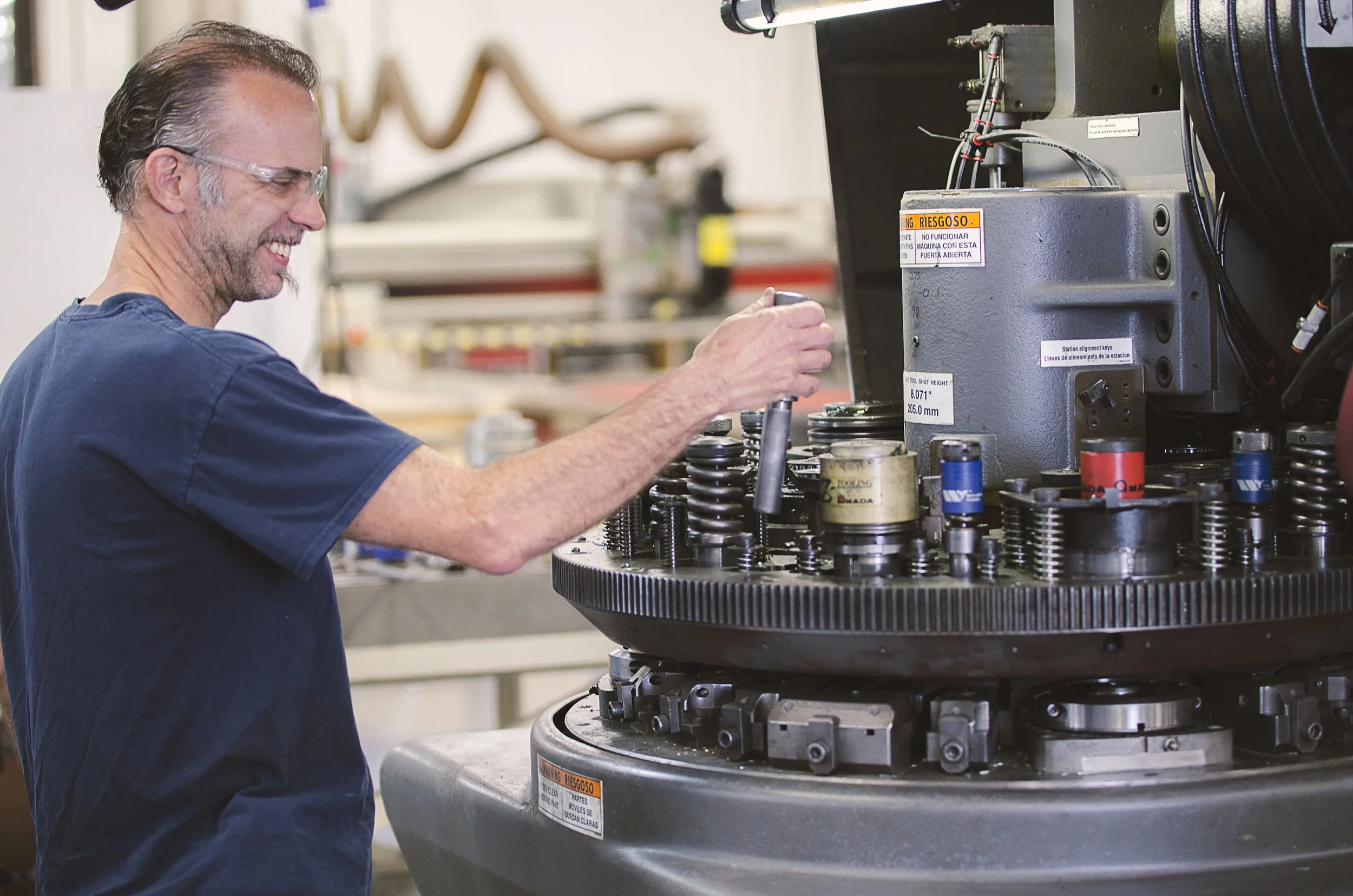 A man wearing glasses and a navy blue shirt working atop a large industrial machine with multiple gears and components.
