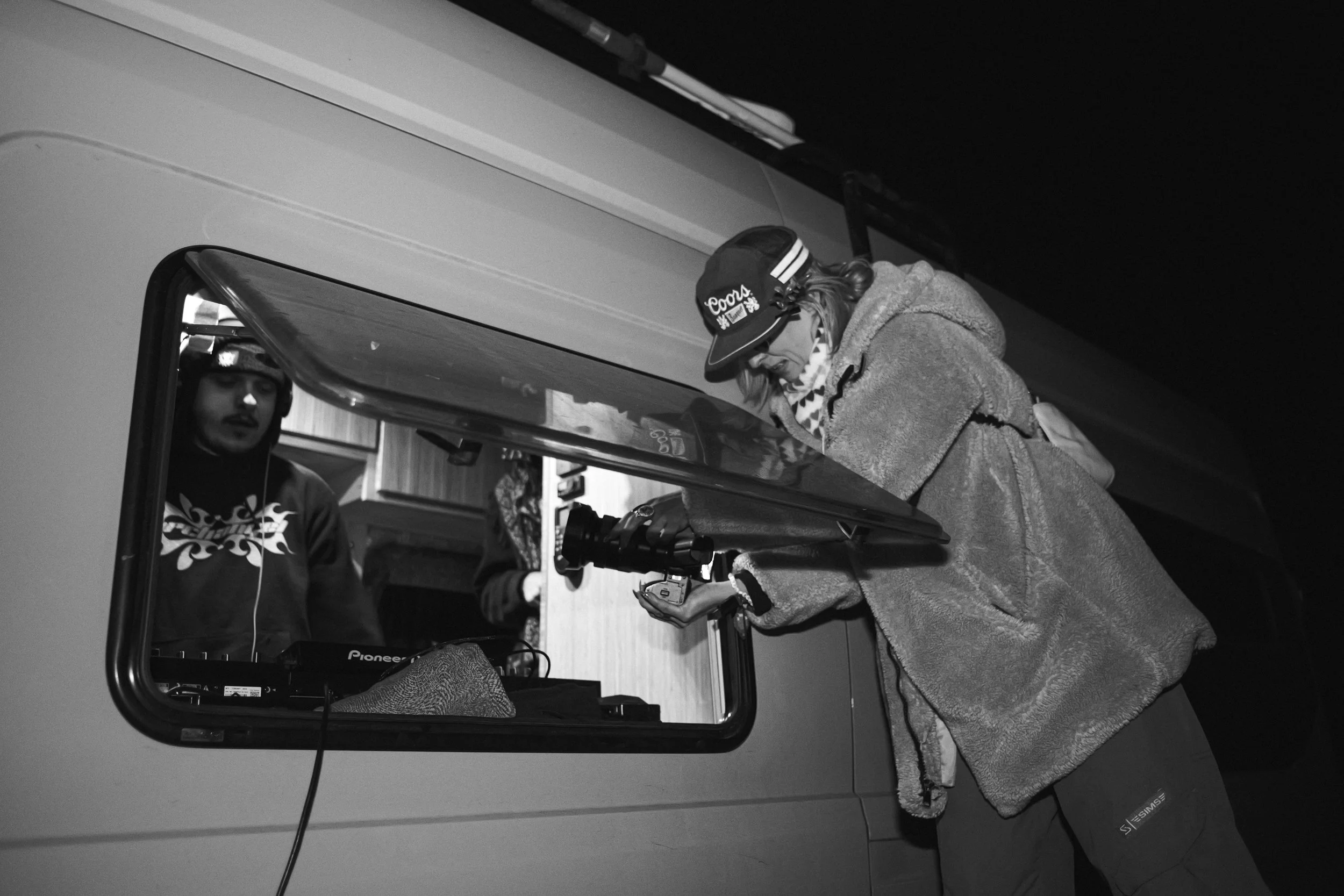 People inside of a bus seen through an open window, with one person outside taking a photo or video.