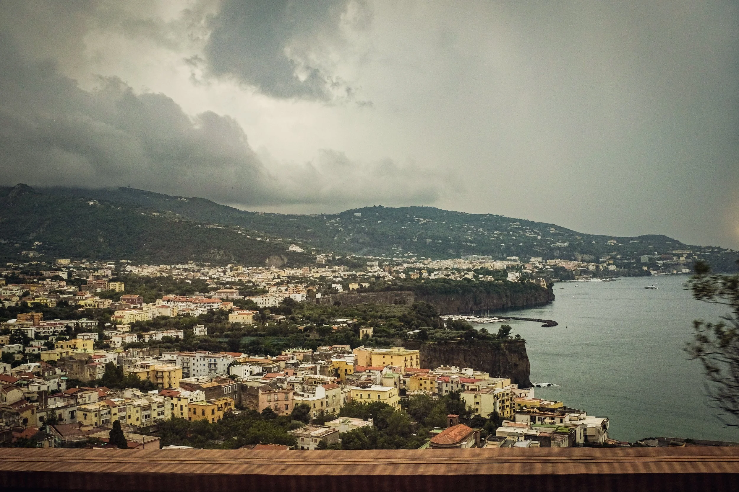 Overcast view of a coastal city with colorful buildings, cliffs, and water, possibly during a storm or on a cloudy day.