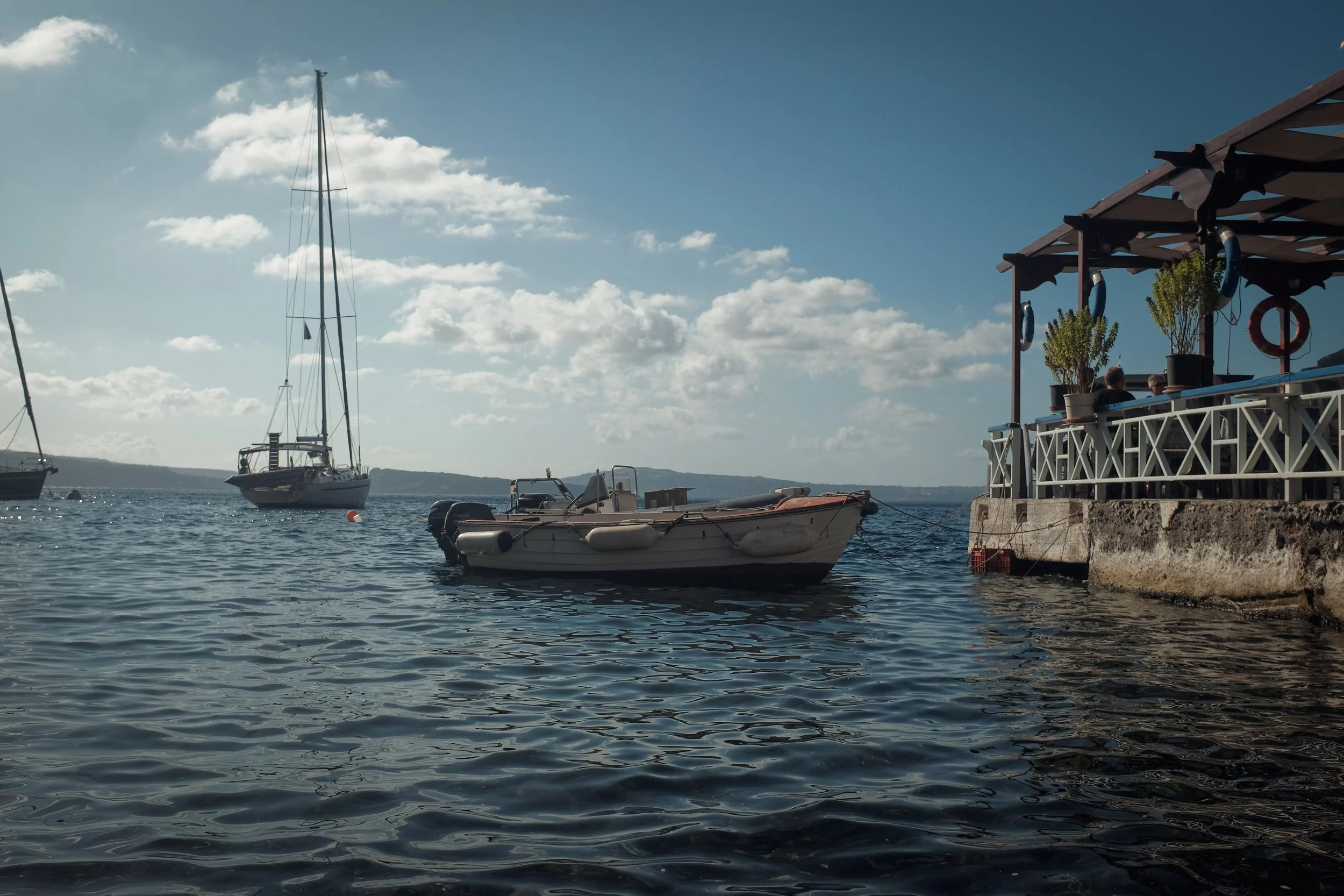 Boats docked by a pier on a sunny day with blue sky and clouds.