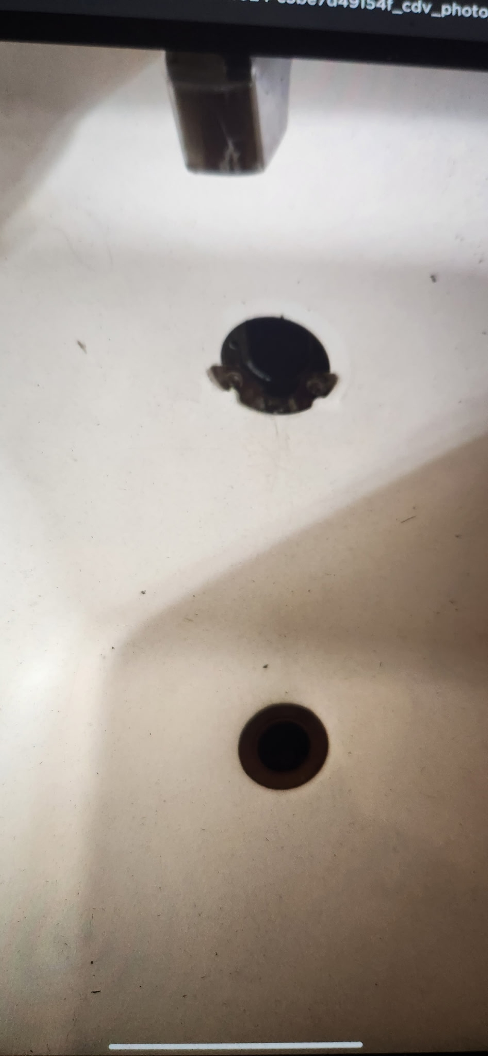 Close-up of a sink with missing faucet or drain cap, showing an empty drain hole and surrounding area.