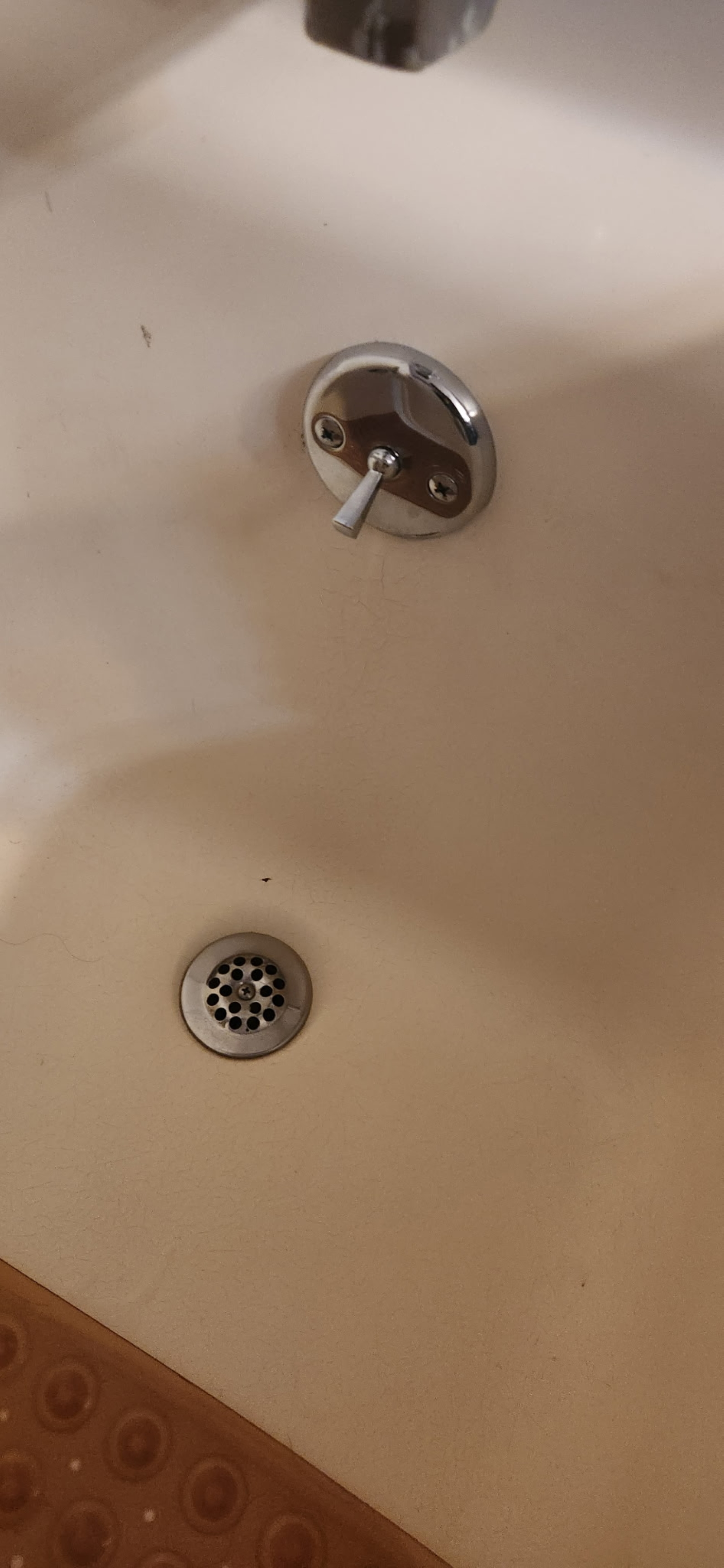Close-up of a bathtub faucet with a lever handle and a drain at the bottom of the tub.