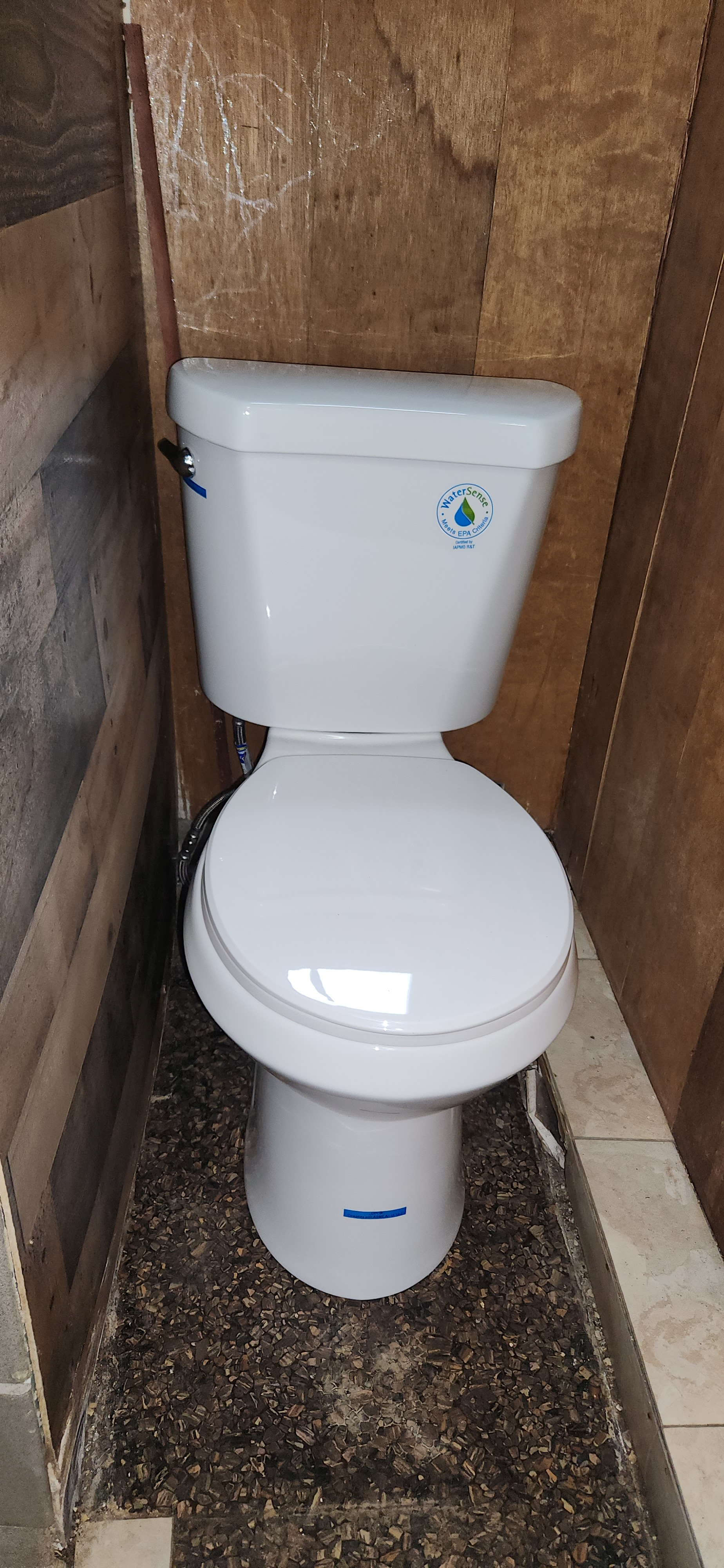 A white water-saving toilet with a label, positioned in a small bathroom with wooden and stone walls and a mosaic tile floor.
