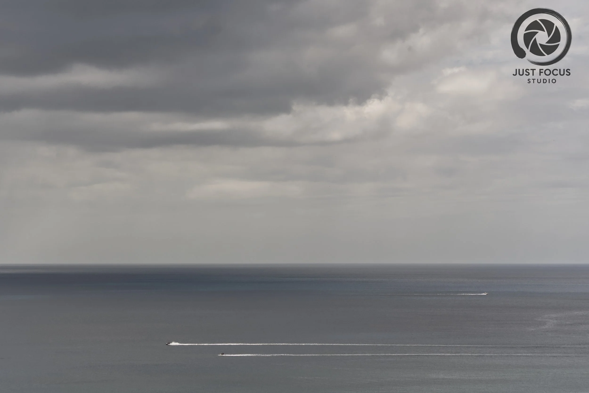Overcast sky over the ocean with three boats creating white trails in the water.
