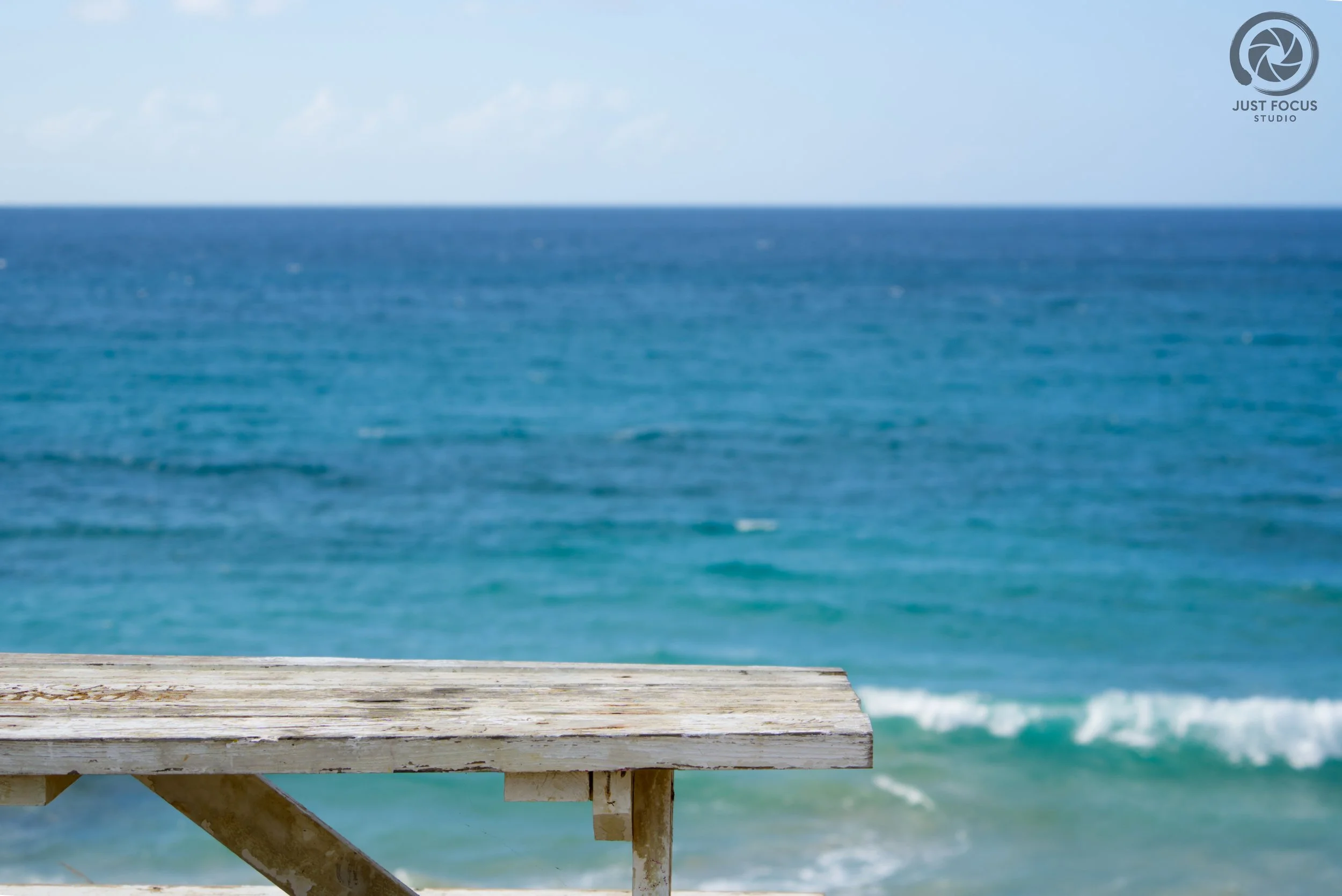Wooden railing in front of a blue ocean with waves and a cloudy sky