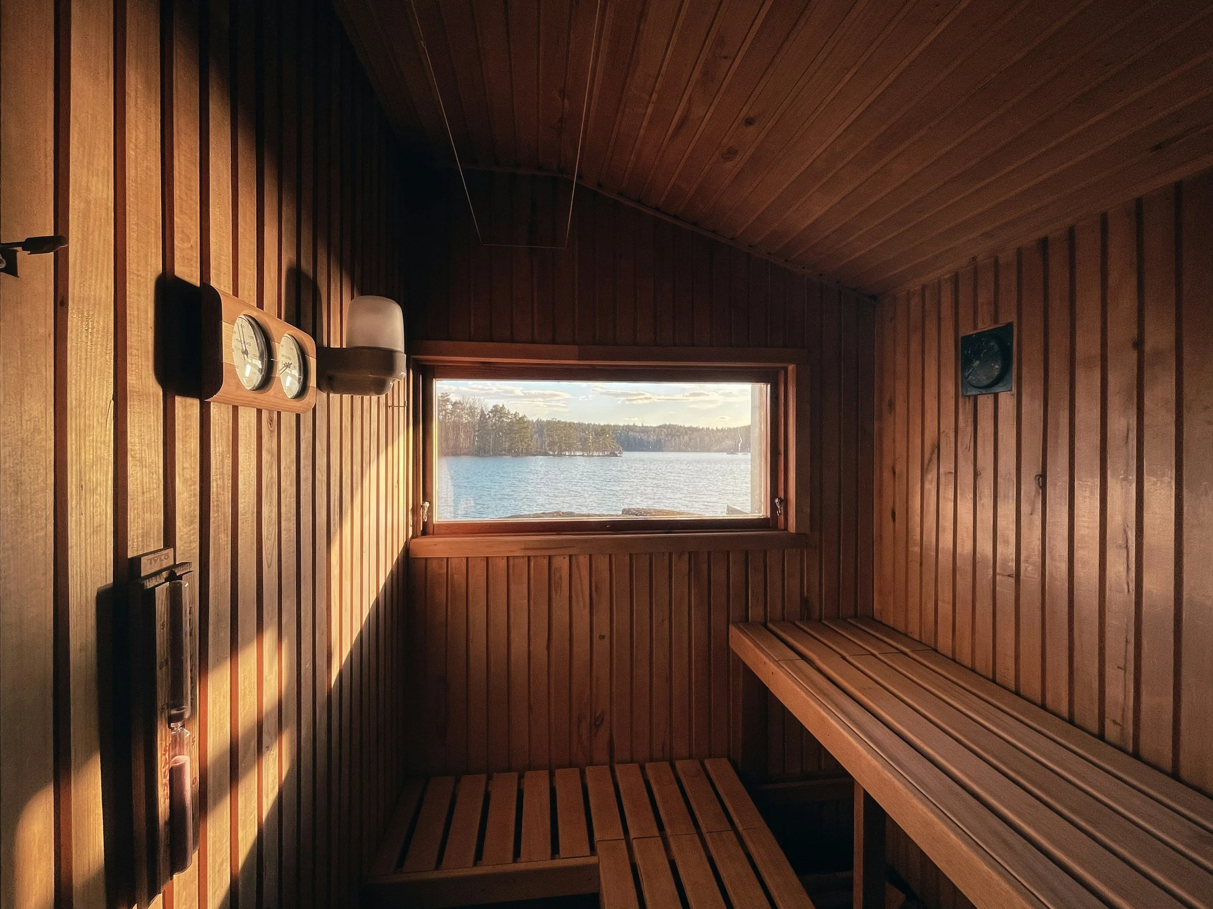Interior of a wooden sauna with a window showing a body of water and trees outside.