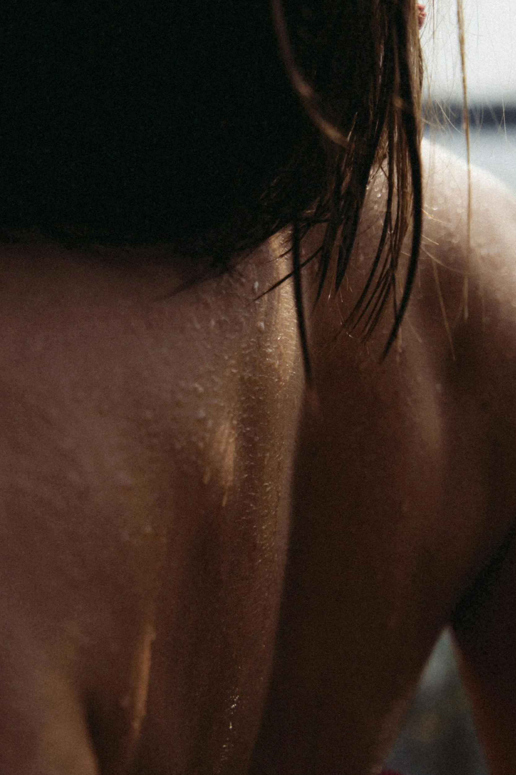 Close-up of a person's shoulder and neck with wet skin and water droplets, with dark hair partially covering the face.