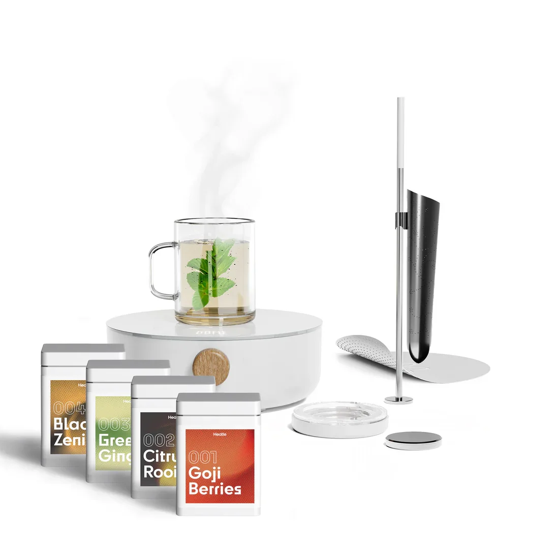 Ein Glas mit heißem Tee, darin ein grünes Blatt, daneben befinden sich vier Teebeutel mit Sorten wie Goji Beeren, Zitronengras, grüner Ingwer und schwarze Zen.