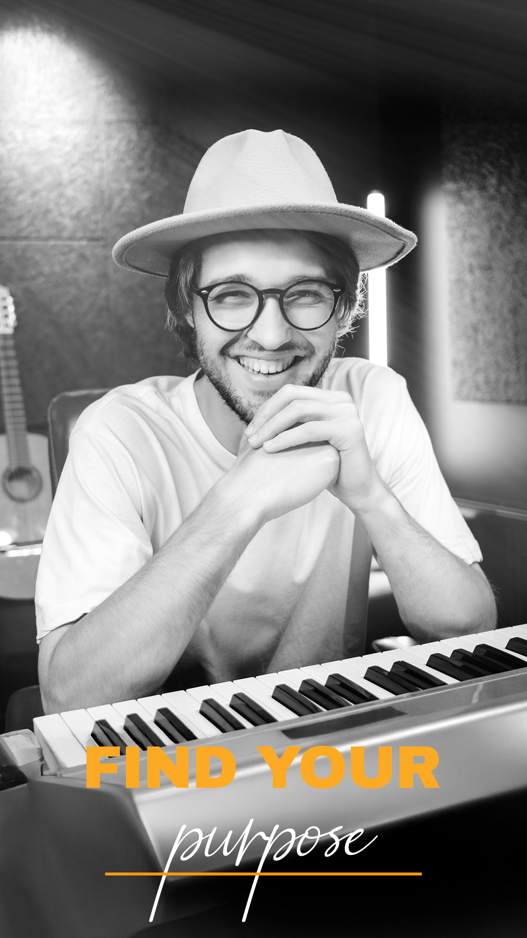 A smiling man with glasses and a hat sitting at a keyboard, with a guitar in the background, in a music studio, with the text "FIND YOUR purpose" overlayed.