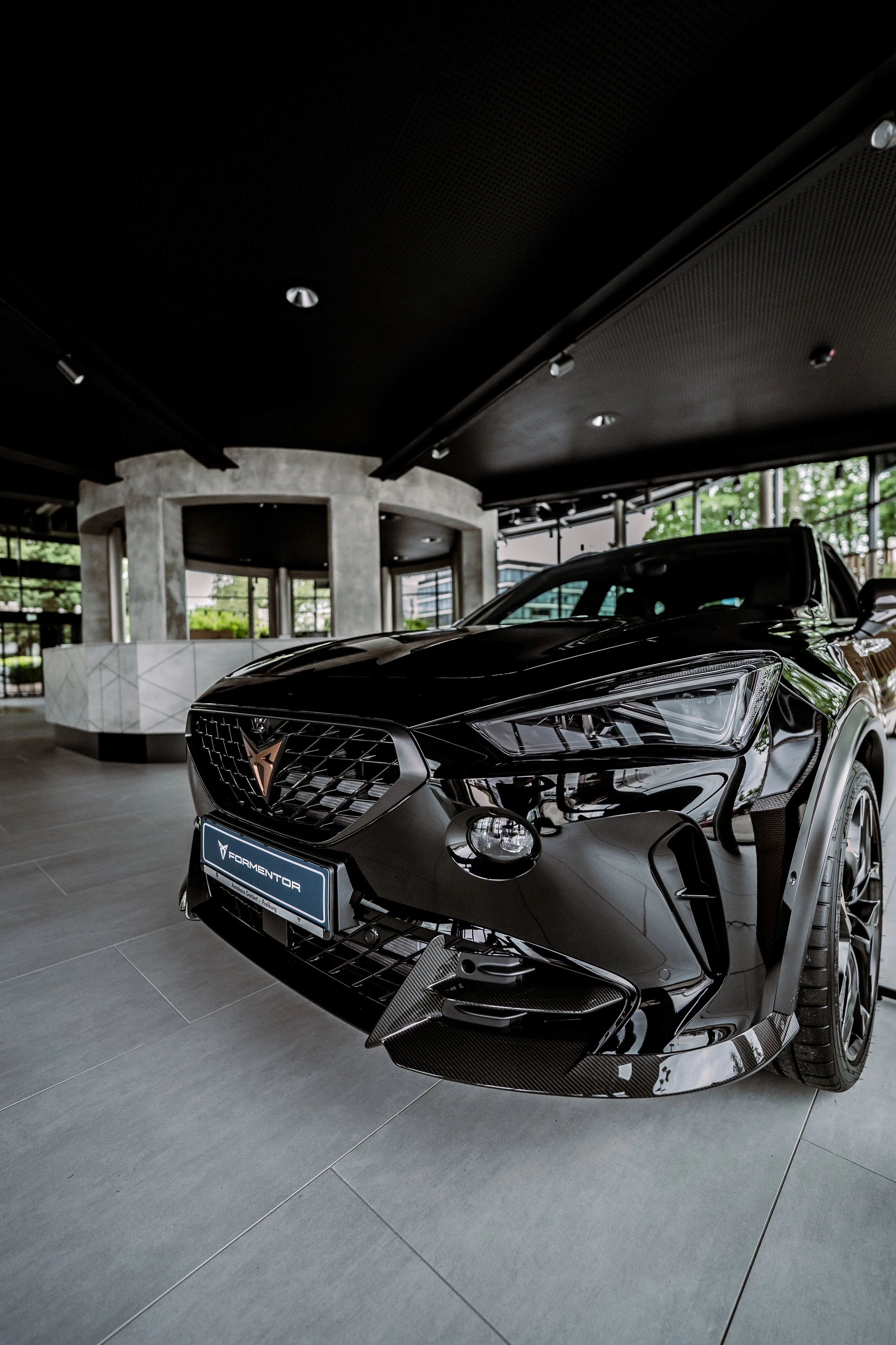 Schwarzer Wagen mit sportlichem Design in einem Showroom, mit sichtbaren Carbon-Elementen am Frontbereich.