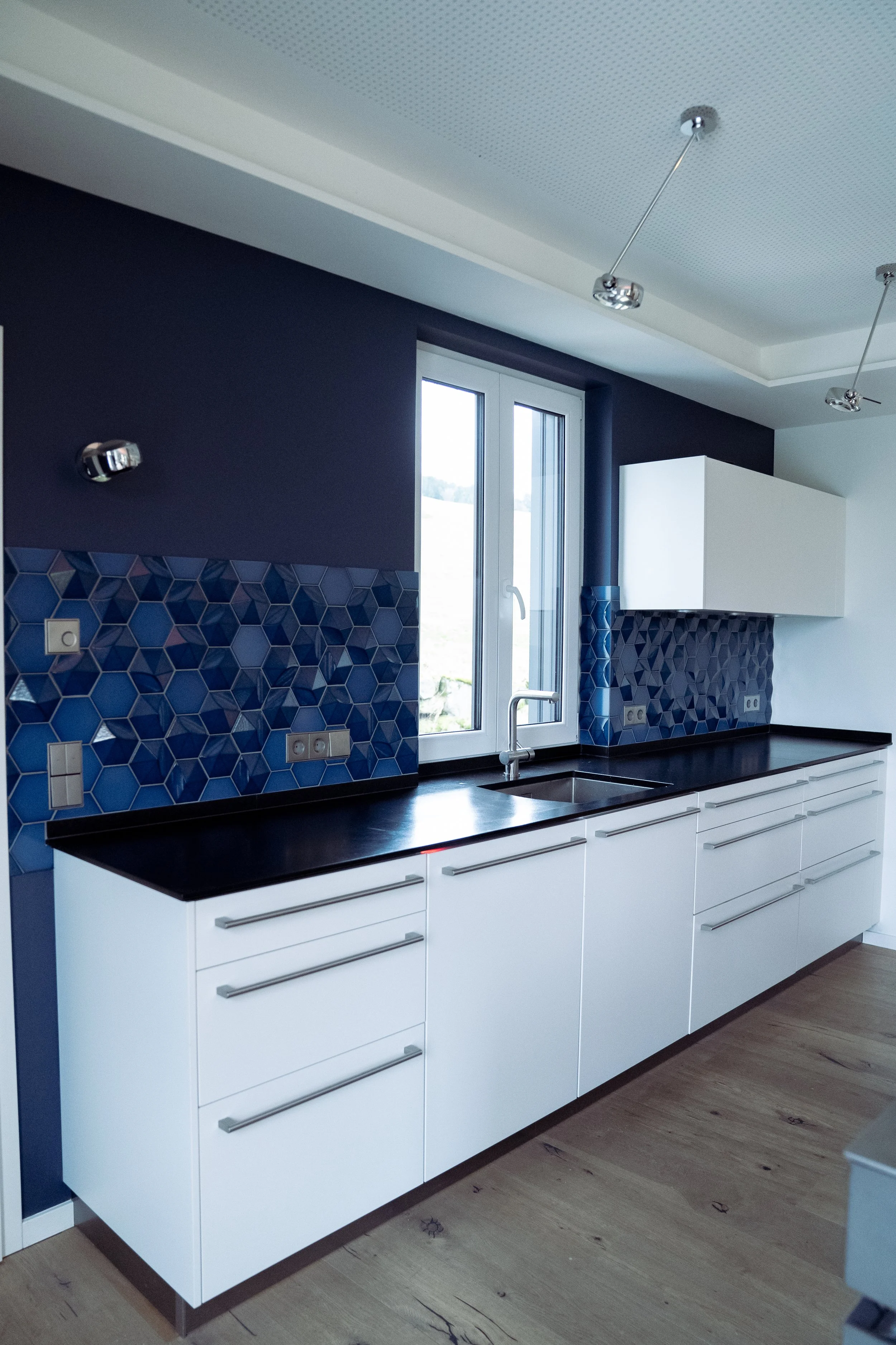 Küchenzeile mit weißen Schränken, schwarzer Arbeitsplatte, blauer Fliesenspiegel und Fenster