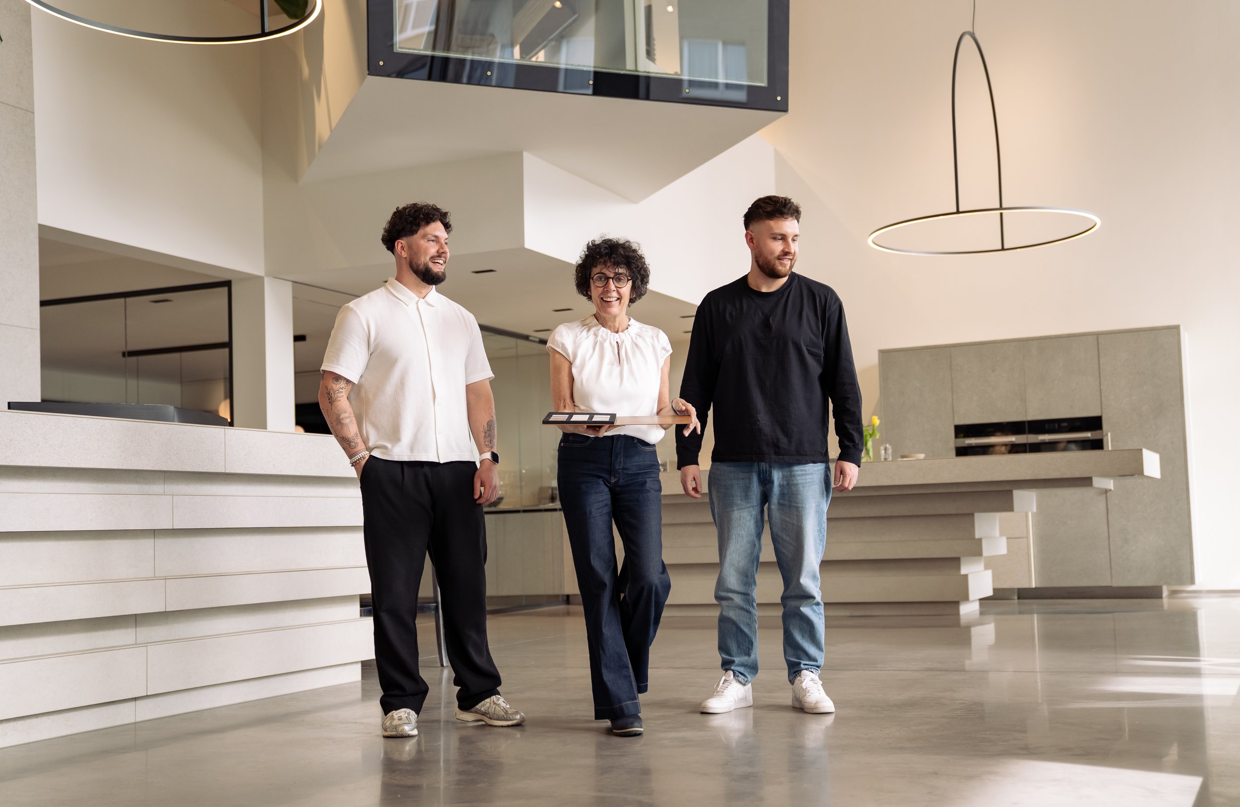 Drei Menschen gehen im modernen, minimalistischen Büro umher, während sie sich gegenseitig unterhalten.