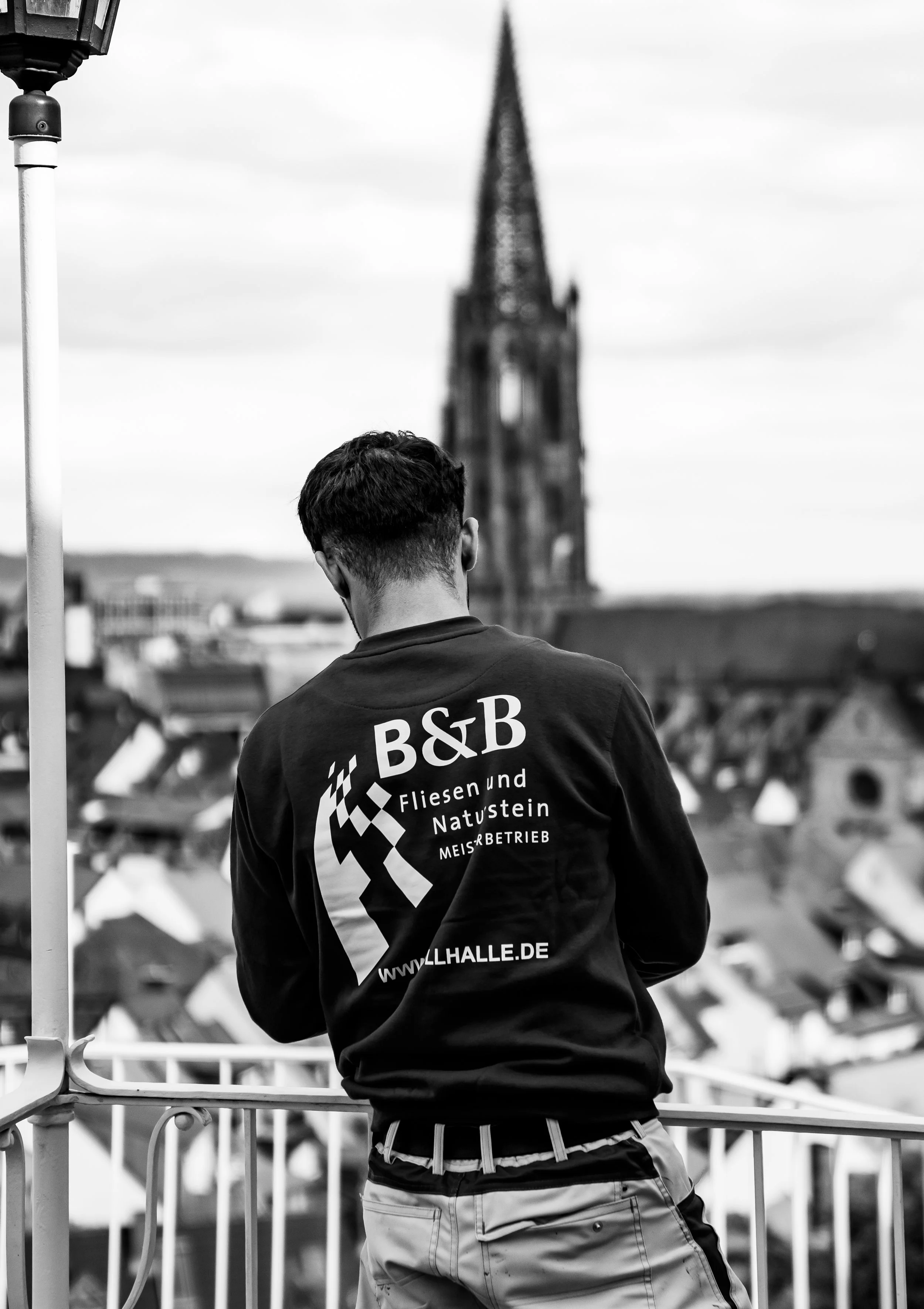 Junge Person schaut auf eine Stadt mit Kirche im Hintergrund, aufgenommen in Schwarz-Weiß.