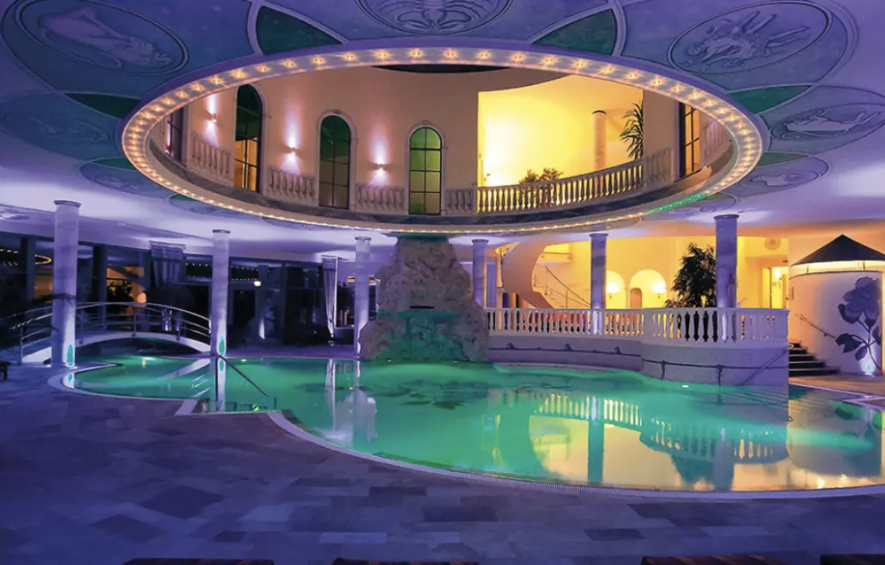 Innenraum mit Pool, gestrichelte Stufen, Säulen, Balkon, und bunte Beleuchtung