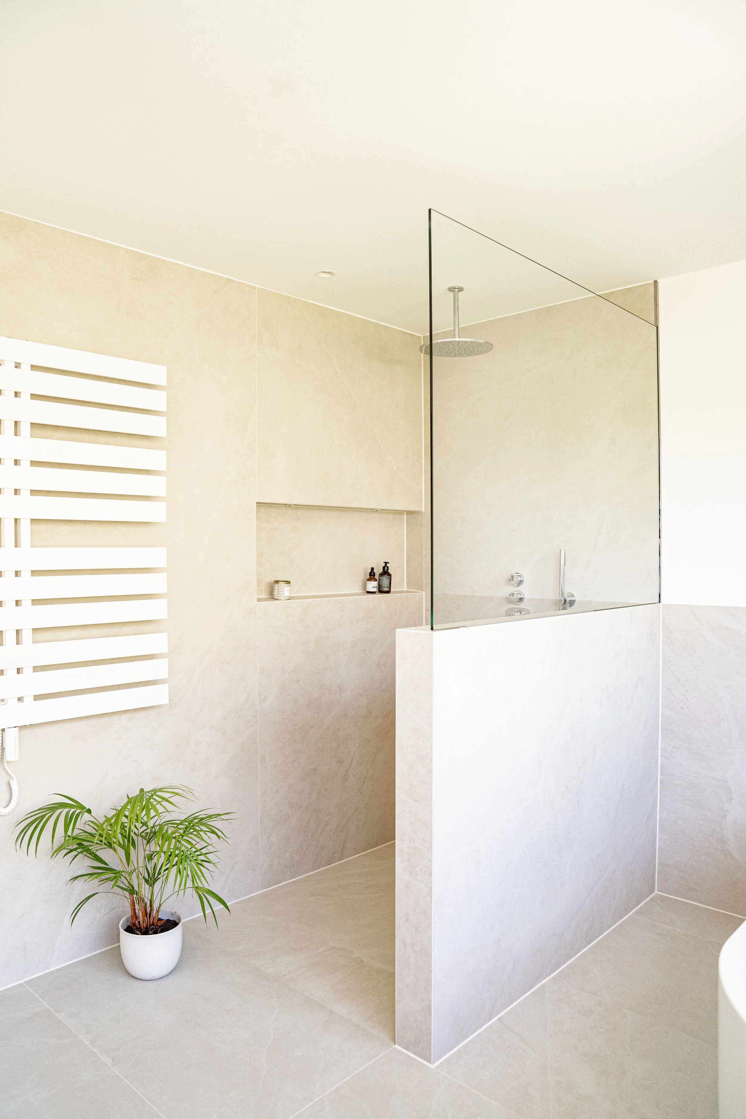 Moderner, minimalistischer Badezimmerbereich mit Dusche, sichtbarer Glastrennwand, Wandheizung und Pflanze in weißem Top.
