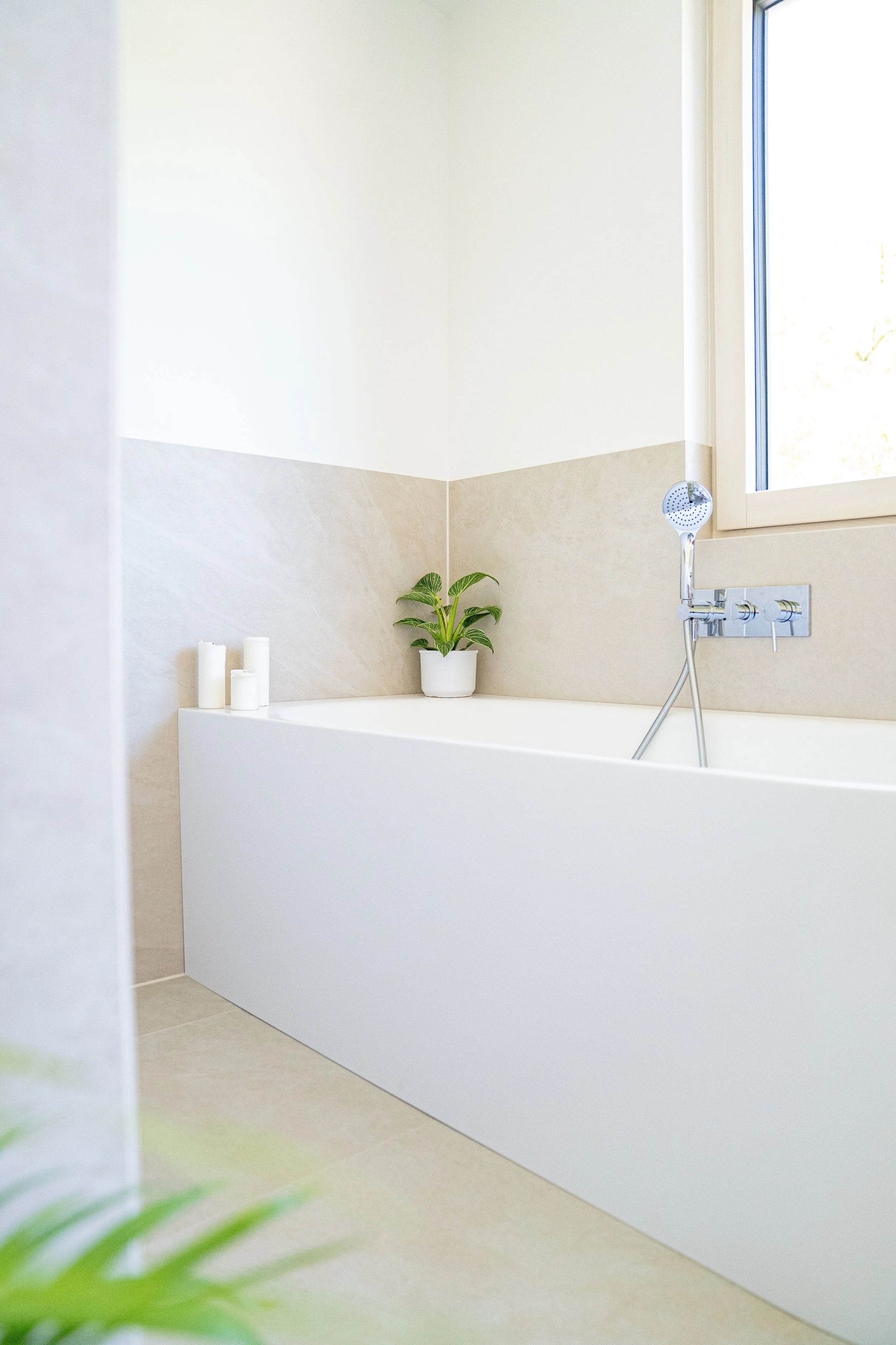 Moderner Badezimmerbereich mit Badewanne, Pflanzen und Kerzen, neben einem Fenster
