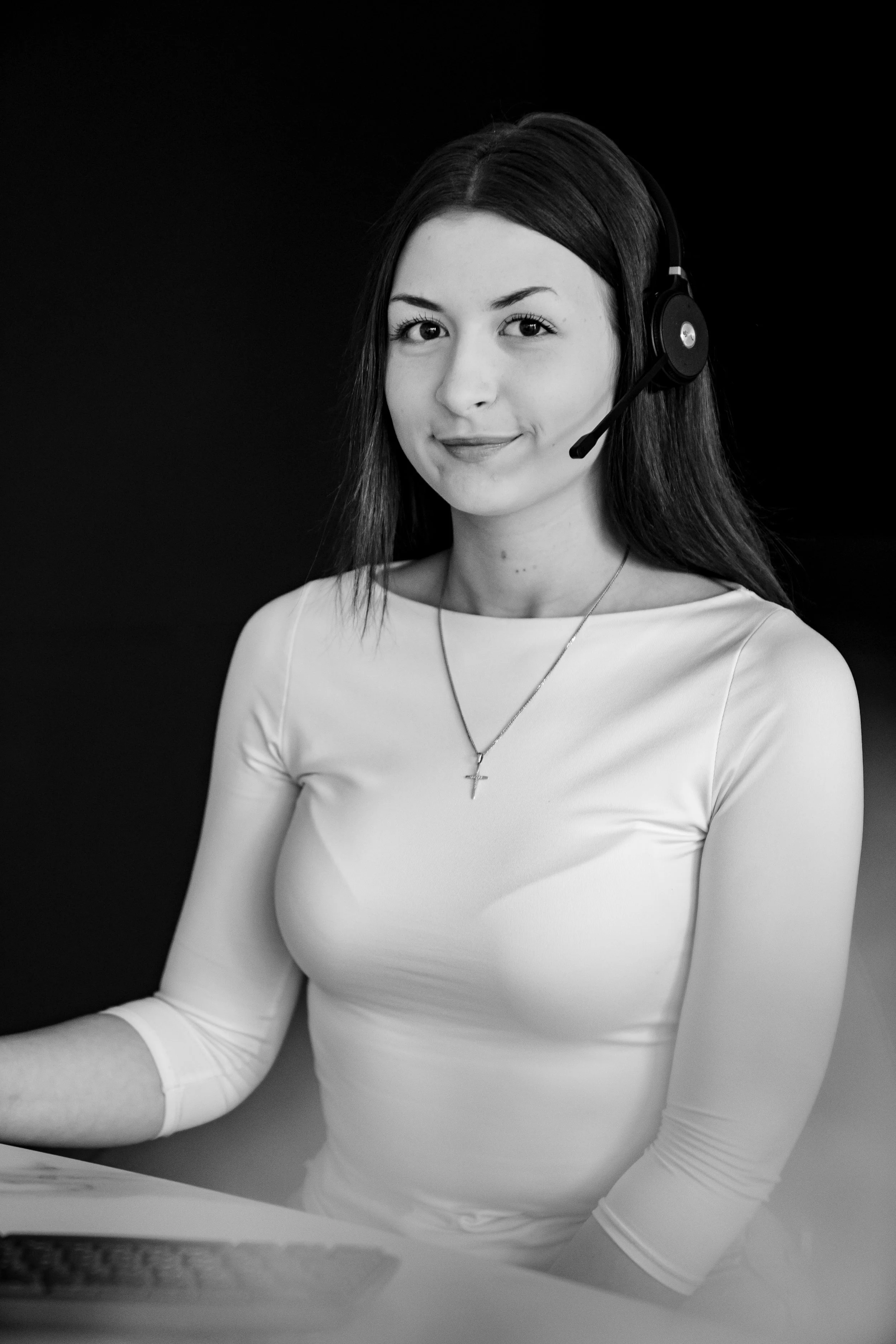 Eine junge Frau trägt einen weißen Oberteil und ein Headset, die auf einem schwarzen Hintergrund sitzt.