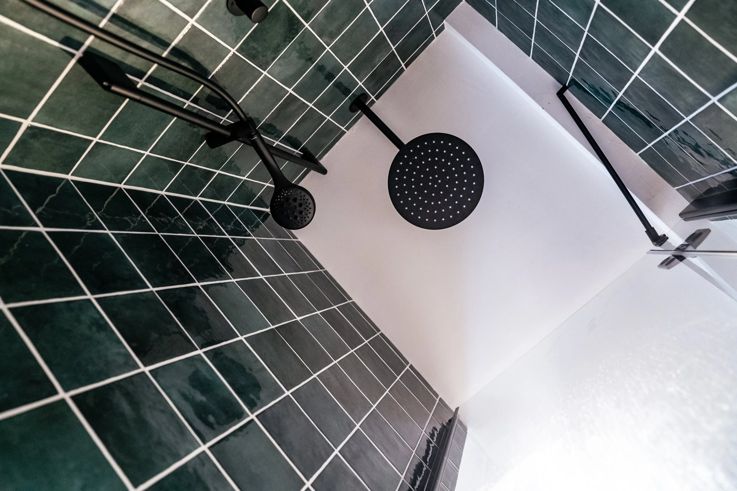 Duschkopf und Handbrause in einer modernen Dusche mit grünen Fliesen.