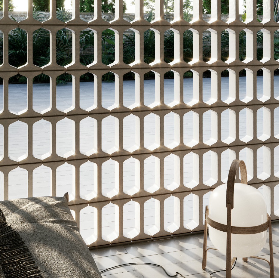 Blick durch ein dekoratives Gitter auf einen Garten mit grünen Pflanzen und beigem Zaun. Im Vordergrund befindet sich ein Sitzkissen und eine weiße Lampe mit Holzrahmen