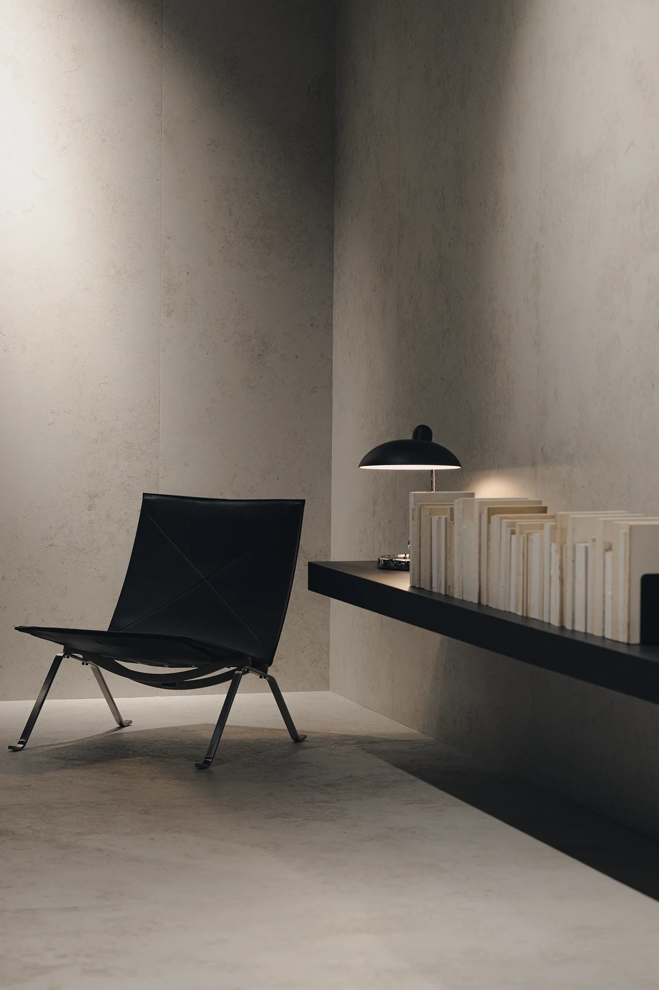 Modernes, minimalistisch eingerichtetes Zimmer mit schwarzem Sessel, dunklem Wandlampe und Regal mit Büchern an der Wand.