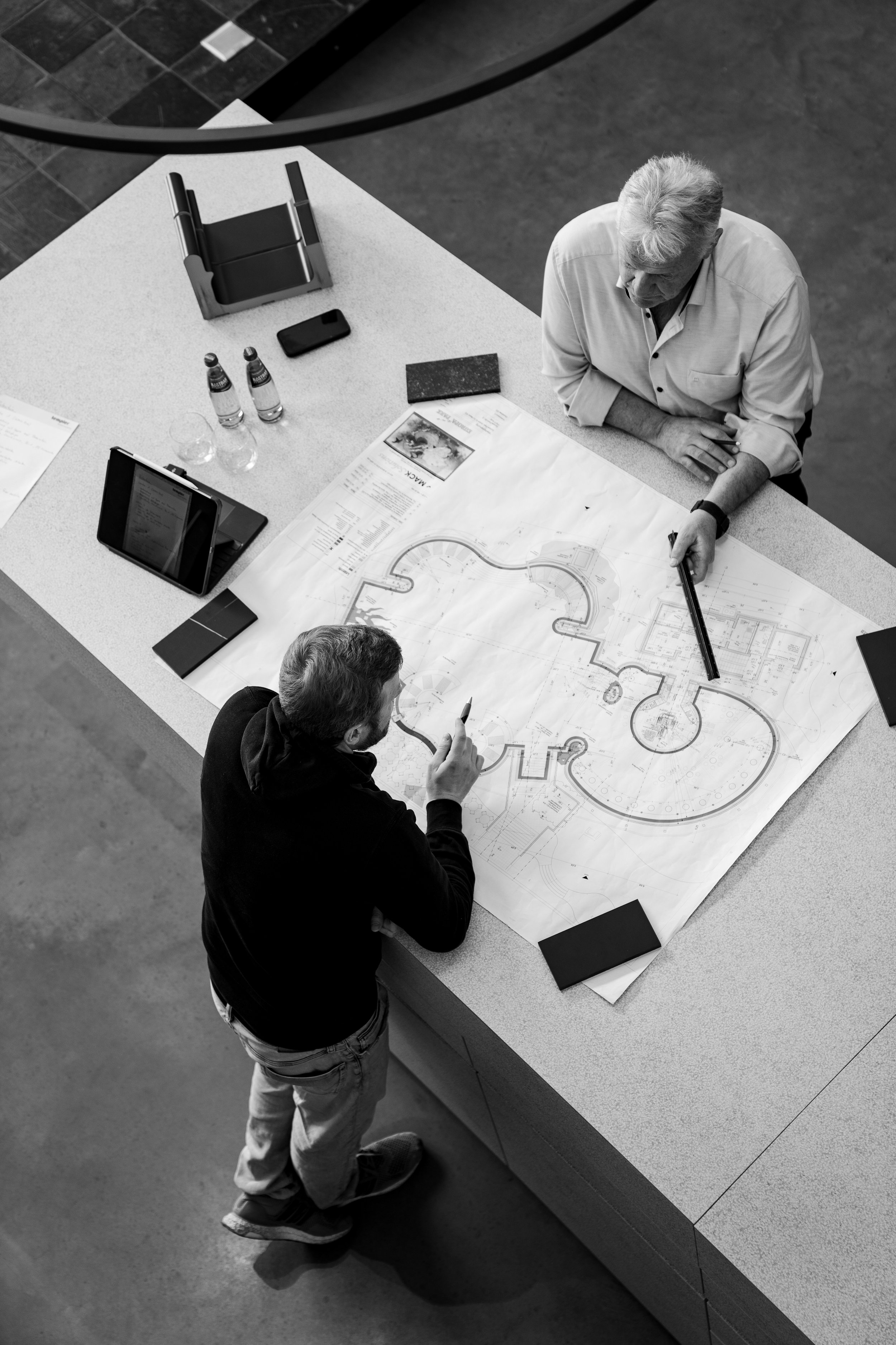 Zwei Männer besprechen einen Bauplan auf einem großen Tisch, der ein Landschafts- oder Architekturprojekt zeigt.
