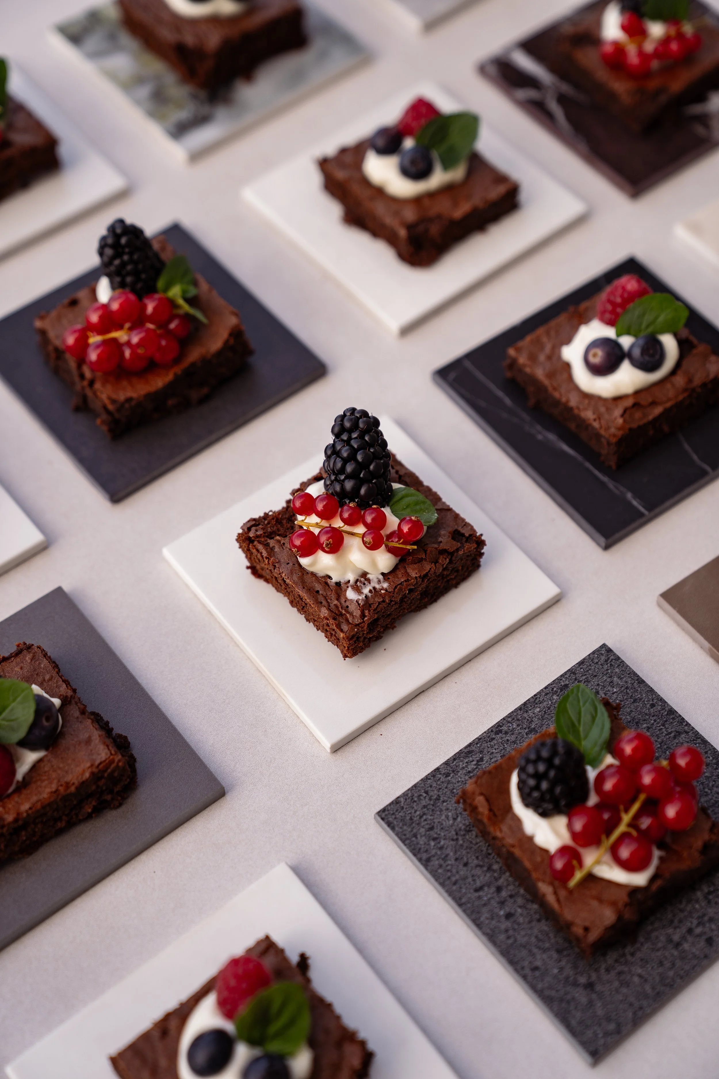 Mehrere Schokoladentorten mit Beeren und Minzblättern, auf quadratischen Platten angerichtet.