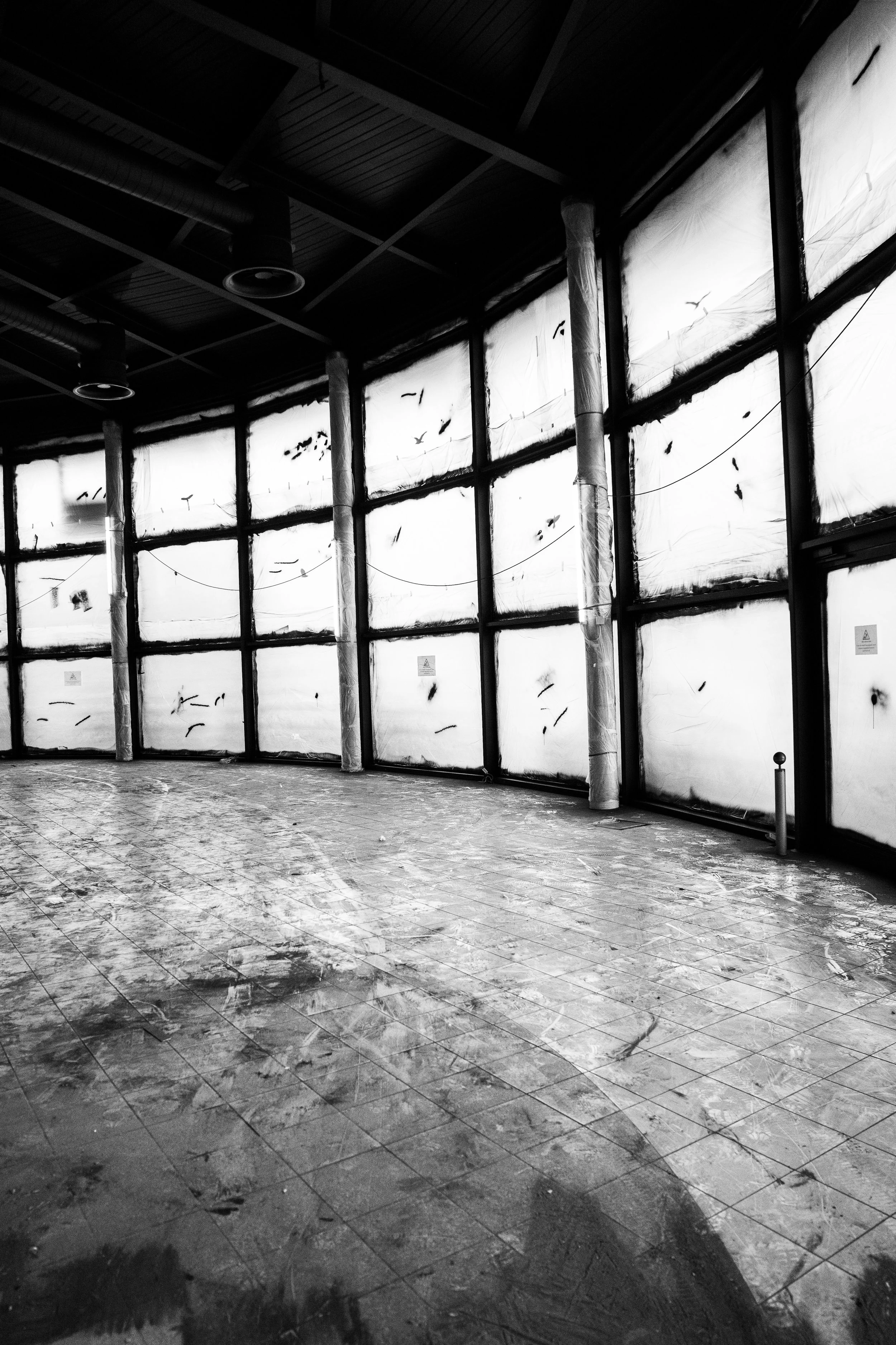 Leeres Gebäude mit großen Fenstern, die mit Plastikfolie abgedeckt sind, und einem verputzten Boden.