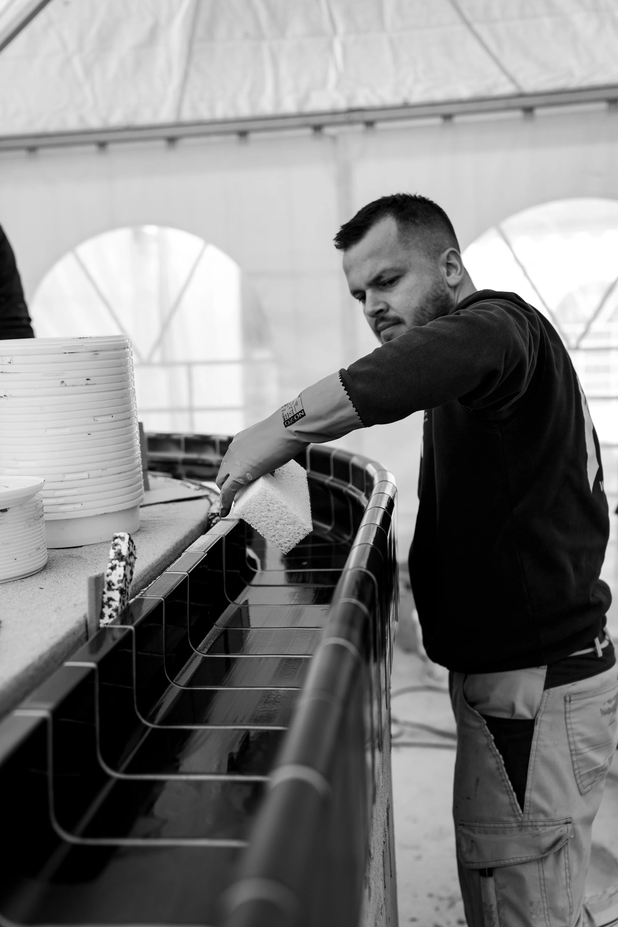 Ein Mann putzt die Oberseite eines langen, rechteckigen Aquariums in einem Zelt. Es sind weiße Töpfe und Requisiten auf dem Rand des Aquariums sichtbar.