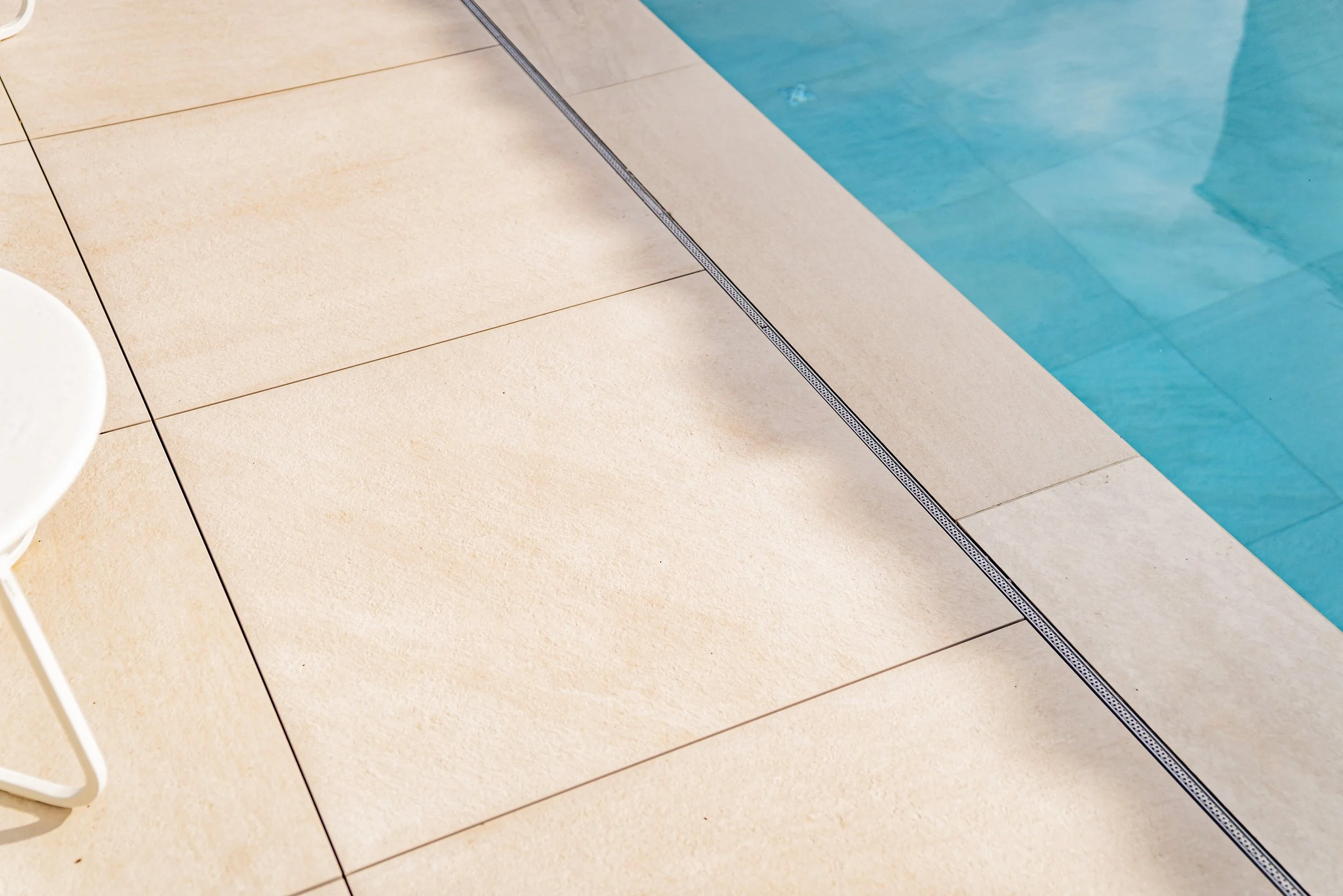 Bodenfliesen am Poolrand mit Wasserabfluss in der Ecke.