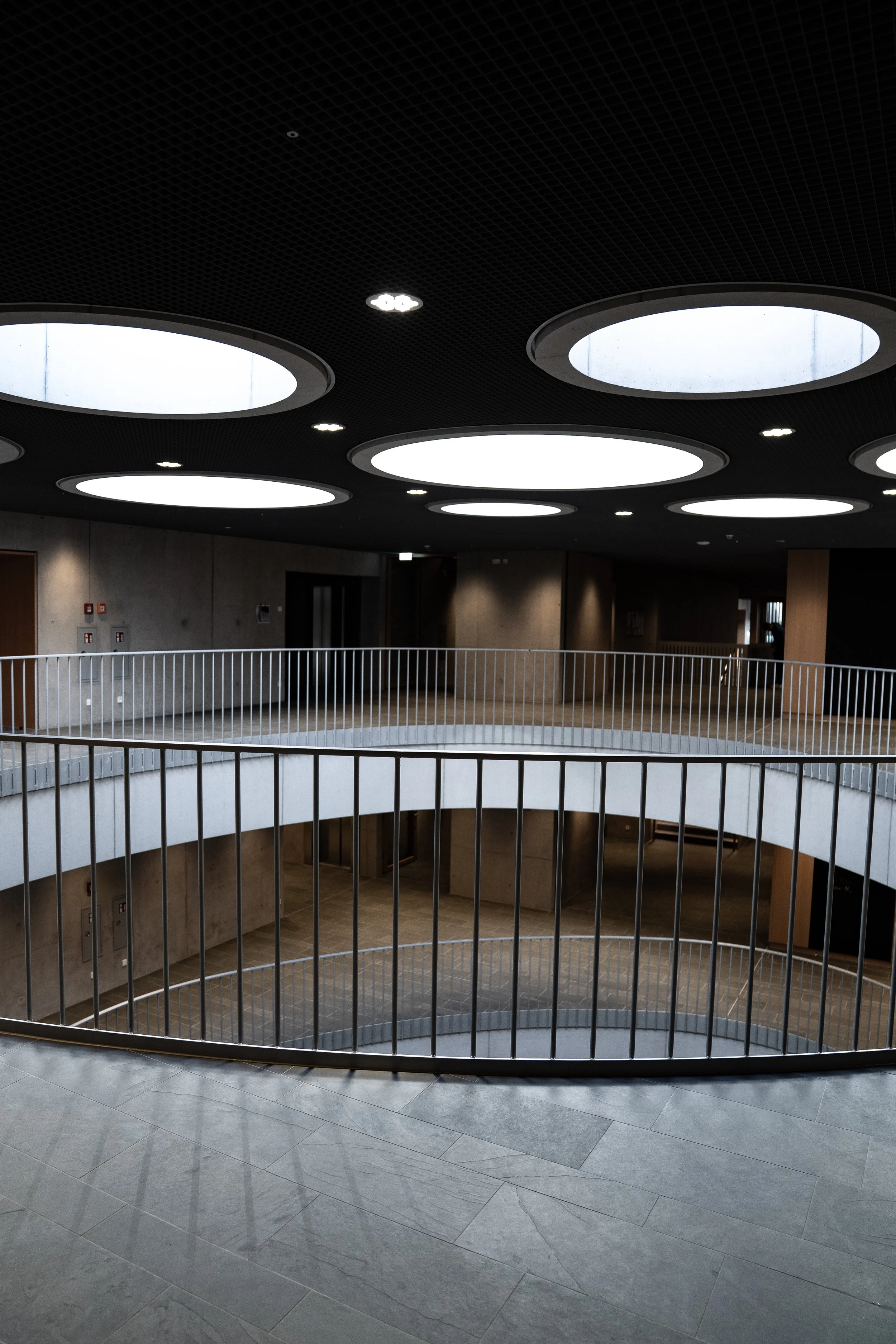 Innenraum eines modernen Gebäudes mit runden Oberlichtern an der Decke, mehrstöckiger Grundriss mit Treppen und Metallgeländern.