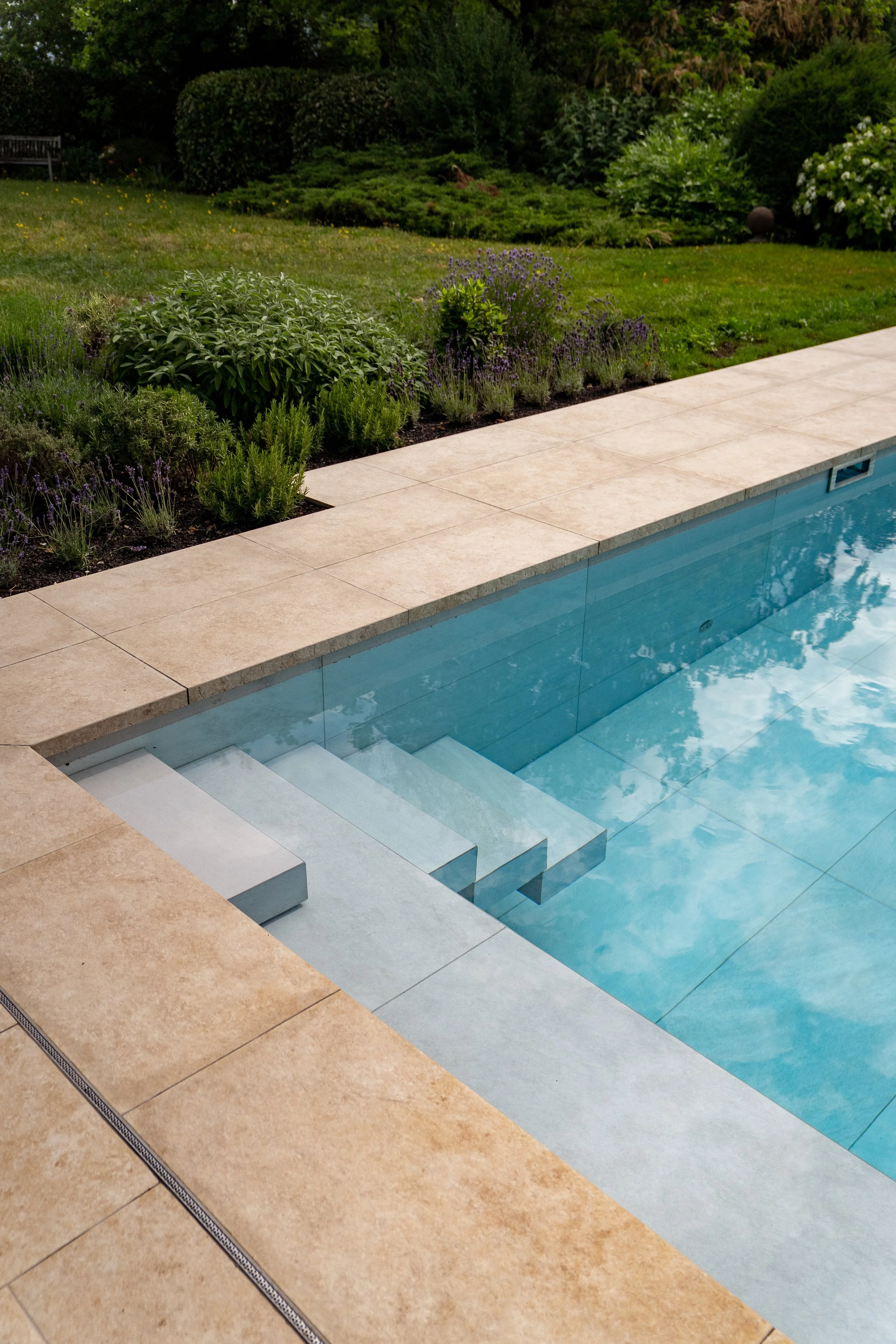 Schwimmbad mit Kieselsteinrand und umliegender Garten mit Blumen und Büschen.