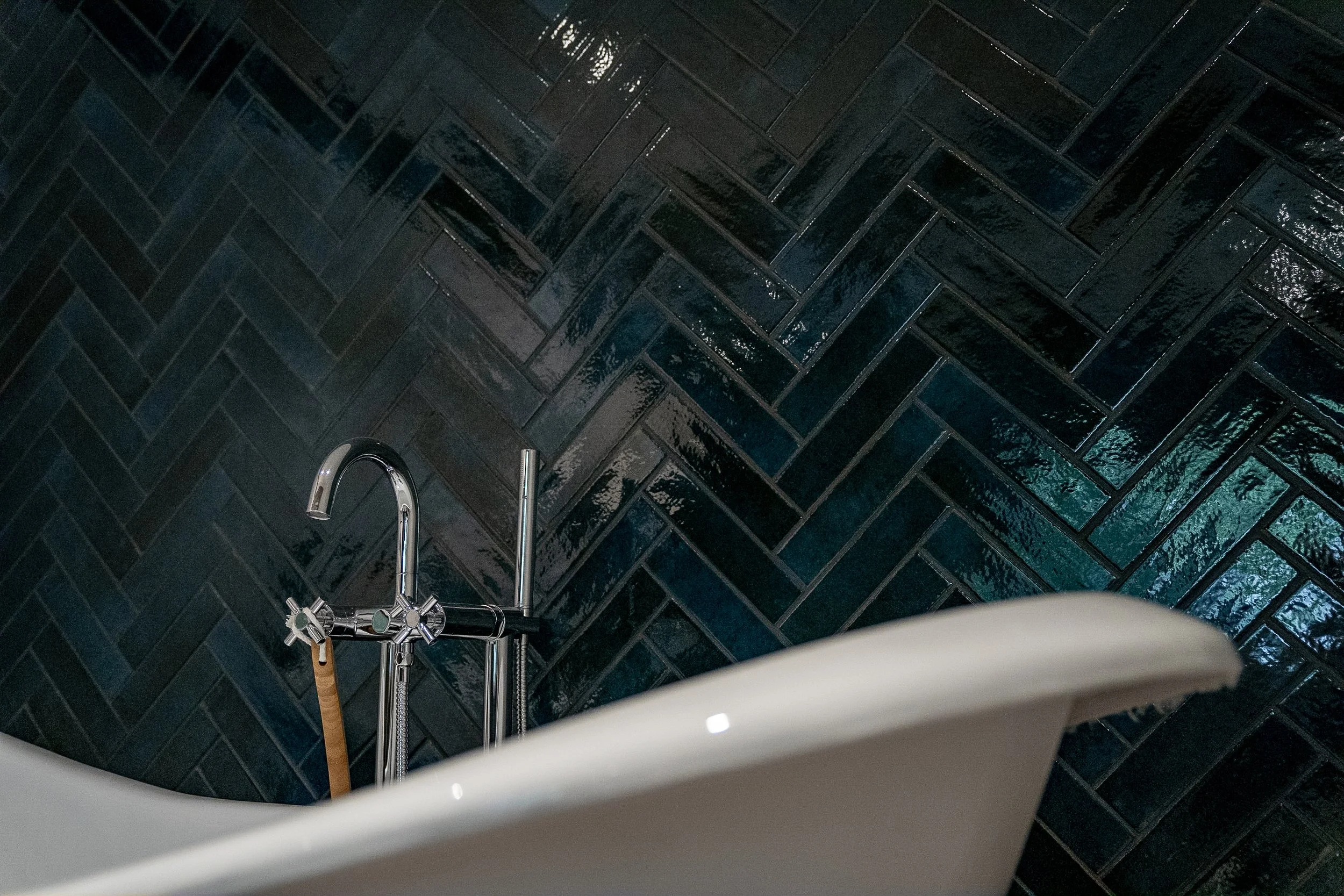 Bodenfliesen in schwarzer, glänzender, diagonaler Fliesenoptik, Blick auf eine Badewanne mit Wasserhahn und Duschstange, dunkler, moderner Badezimmerboden.