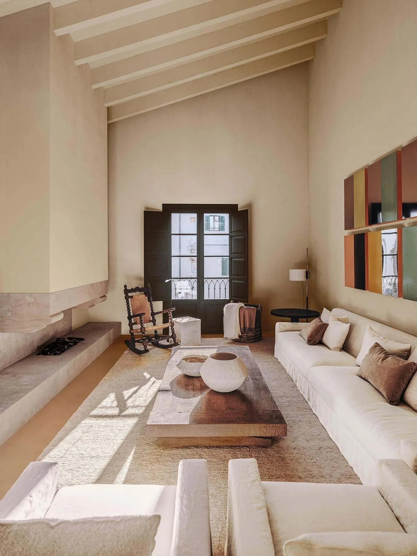 Wohnzimmer mit weißem Sofa, Holztisch, Kamin, Sessel, Stehlampe, Wandregal, Balkon mit Fenstertür, Sonnenlicht, neutralen Farbtönen.