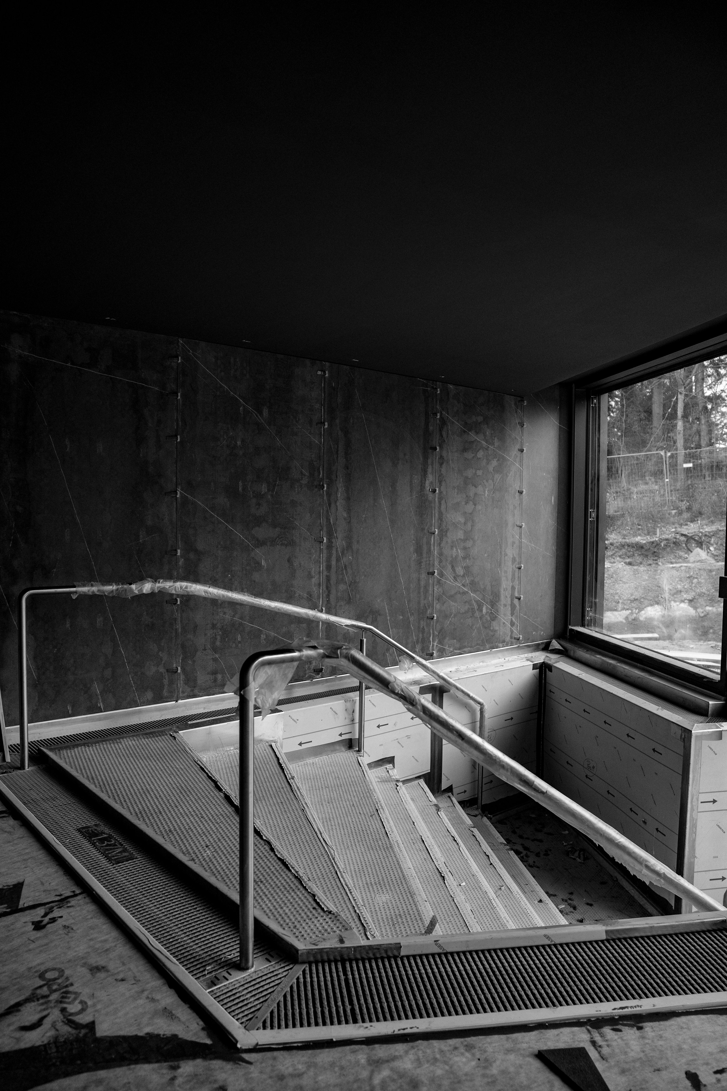 Innenansicht eines modernen Schwimmbads mit laufender Bauarbeit, noch nicht gefüllt, mit Metalltreppe und Fenster an der rechten Seite.