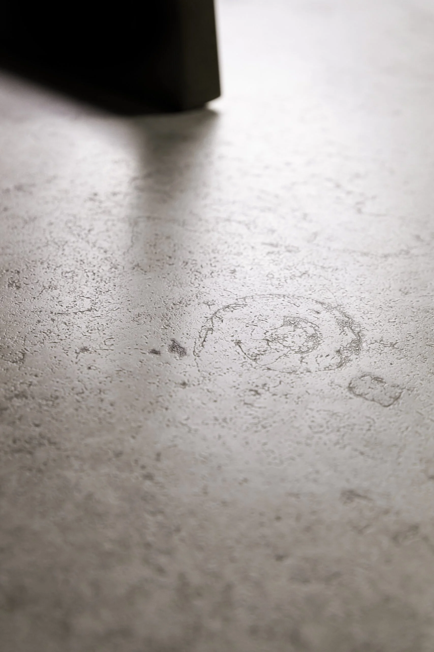 Der Blick auf einen Betonboden, auf dem ein Schuhabdruck einer Person sichtbar ist.