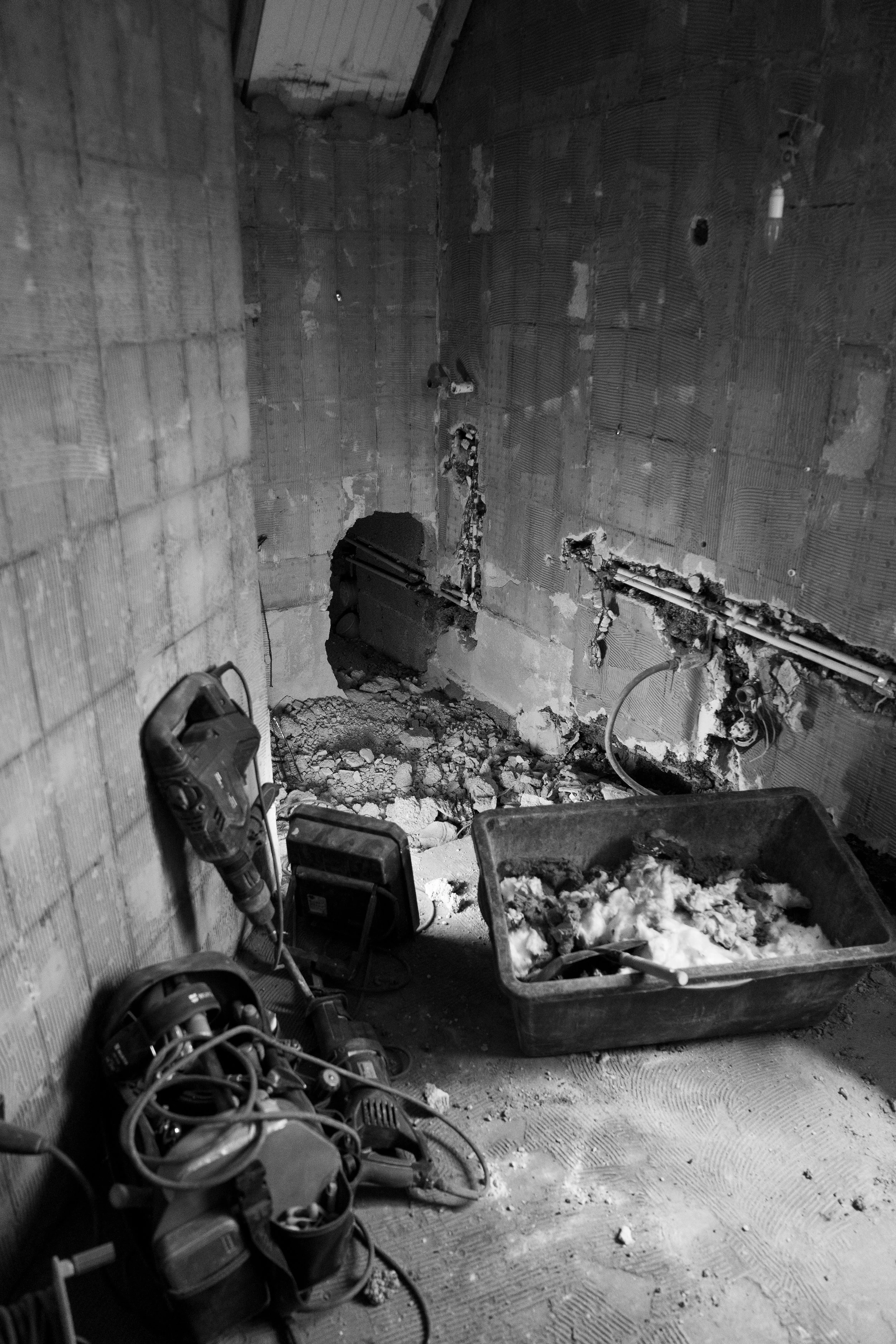 Ein Raum unter Bauarbeiten, mit Werkzeugen und Baumaterialien am Boden, ungeputzte Wände, die Steckdosen und Rohre zeigen.