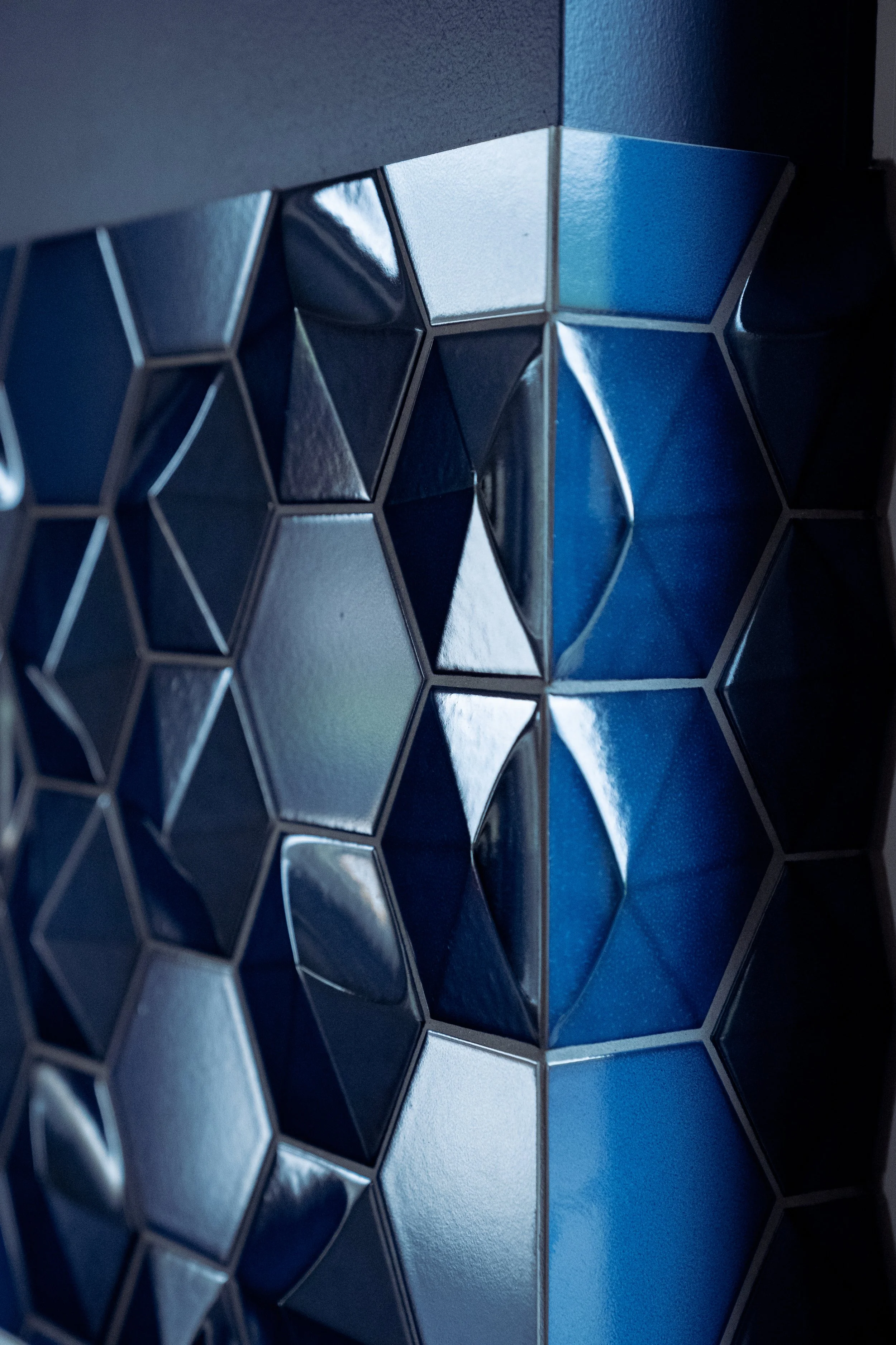 Nahaufnahme eines Hauses mit einer Fassade aus reflektierenden, metallicfarbenen, sechseckigen Fliesen in verschiedenen Blautönen.