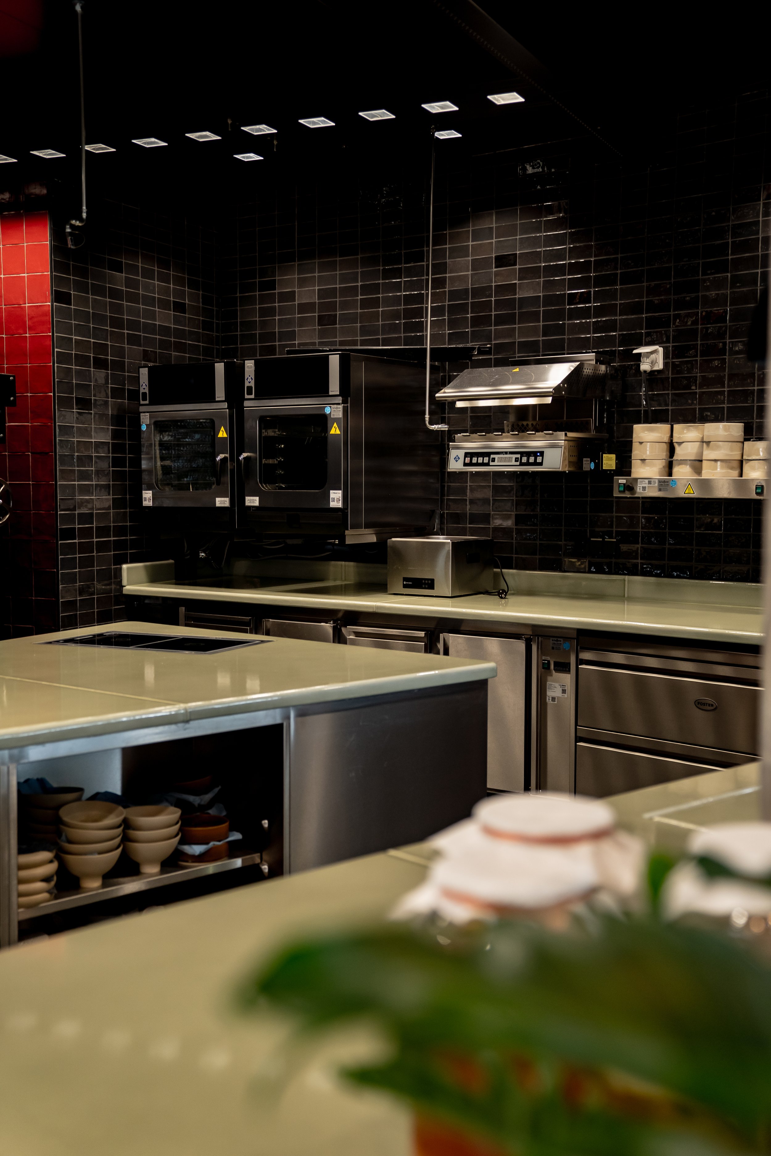 Küchenbereich mit Backofen, Mikrowelle, Dunstabzugshaube, Kühlschrank, Arbeitsflächen und Geschirr, in einem Restaurant oder Café.