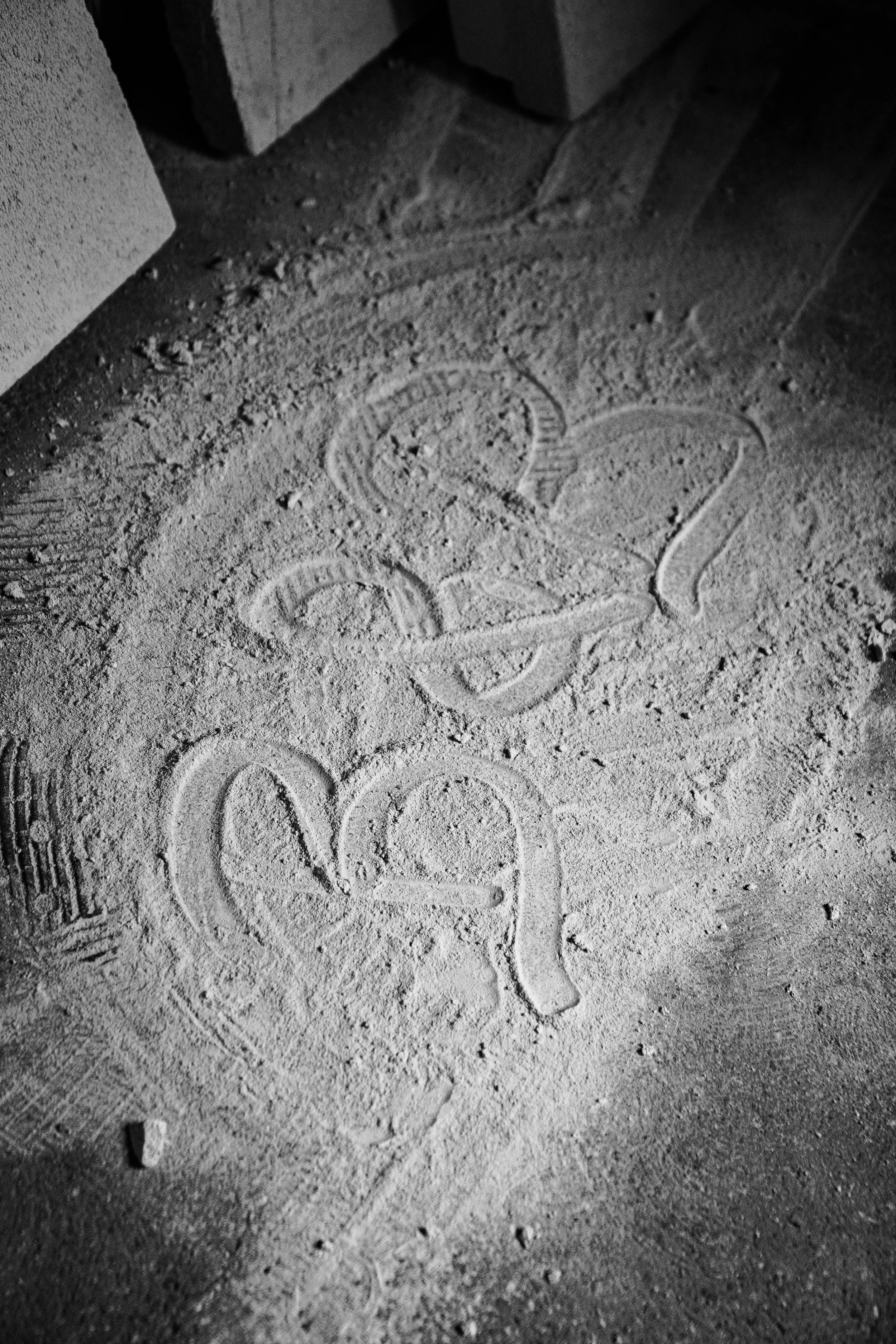 In den Staub auf dem Boden sind verschiedene Zeichnungen und Worte eingraviert, unter anderem ein Herz und das Wort 'LOVE'.