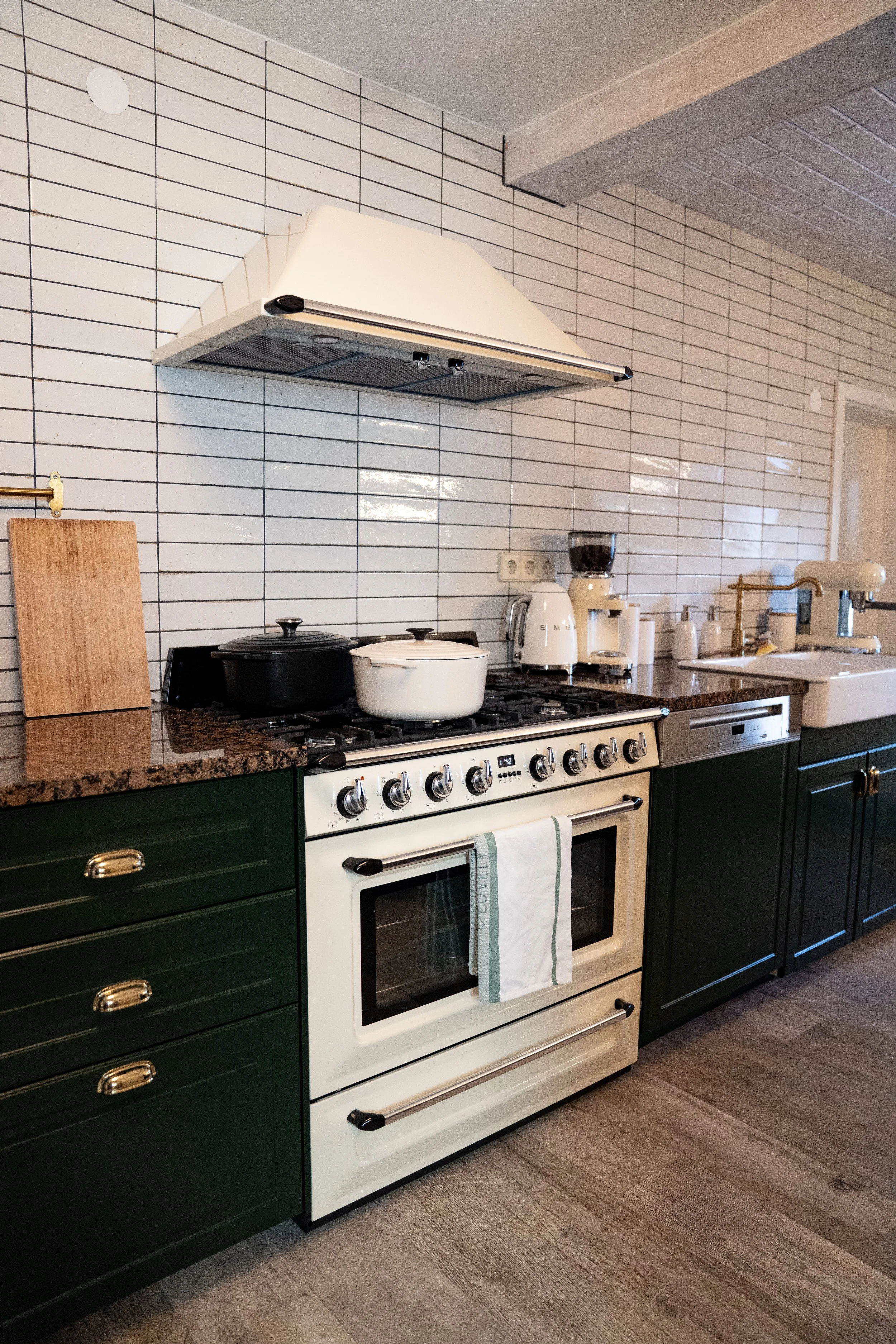 Moderne Küche mit weißen Fliesen, grünen Schränken, Herd mit zwei Töpfen, Küchenutensilien und Waschbecken.