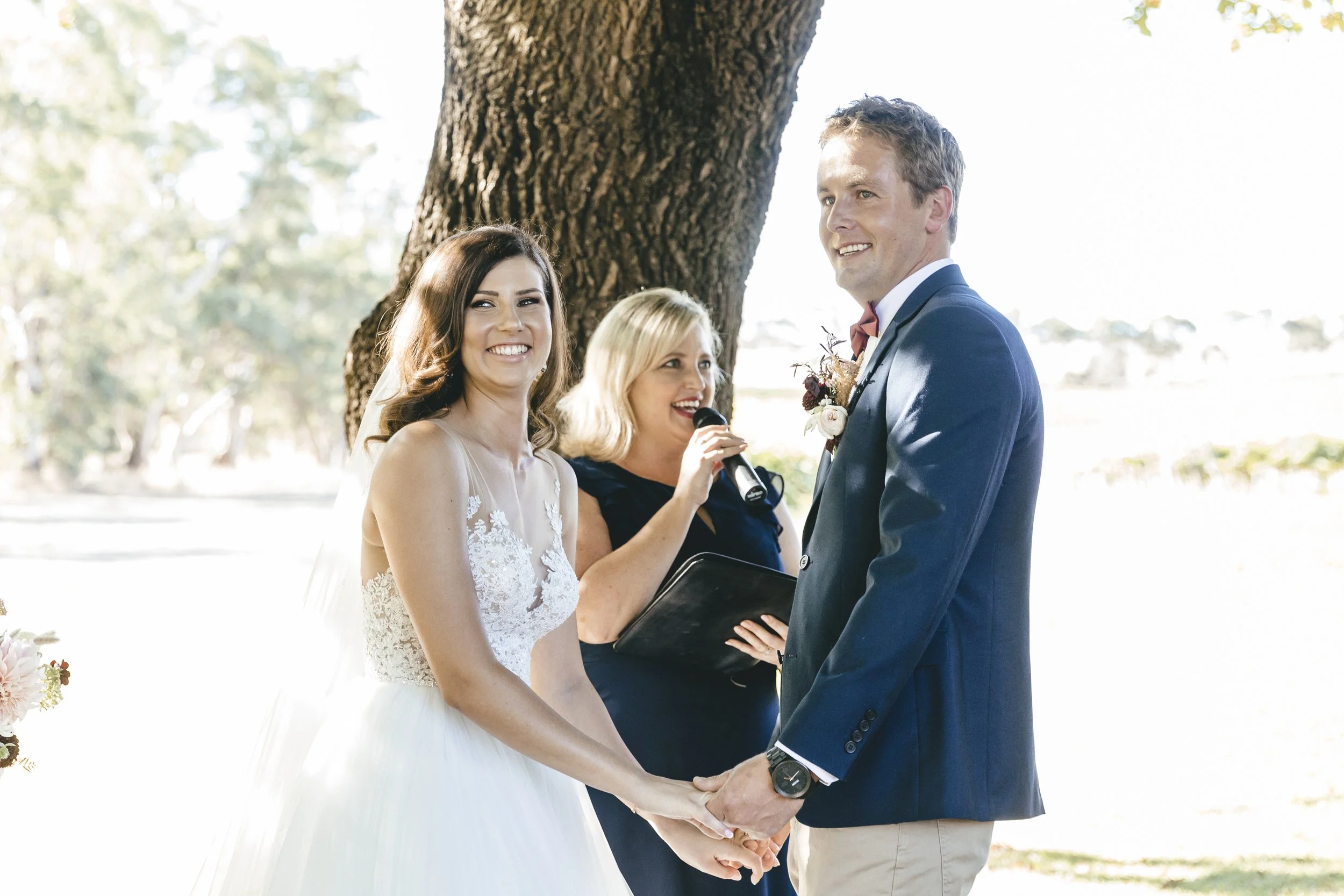 A wedding celebrant holding a microphone in between a couple holding hands