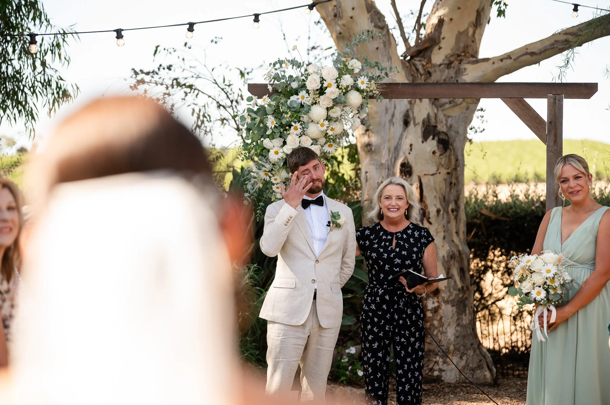 A groom wiping tears at his wedding ceremony standing next to his celebrant